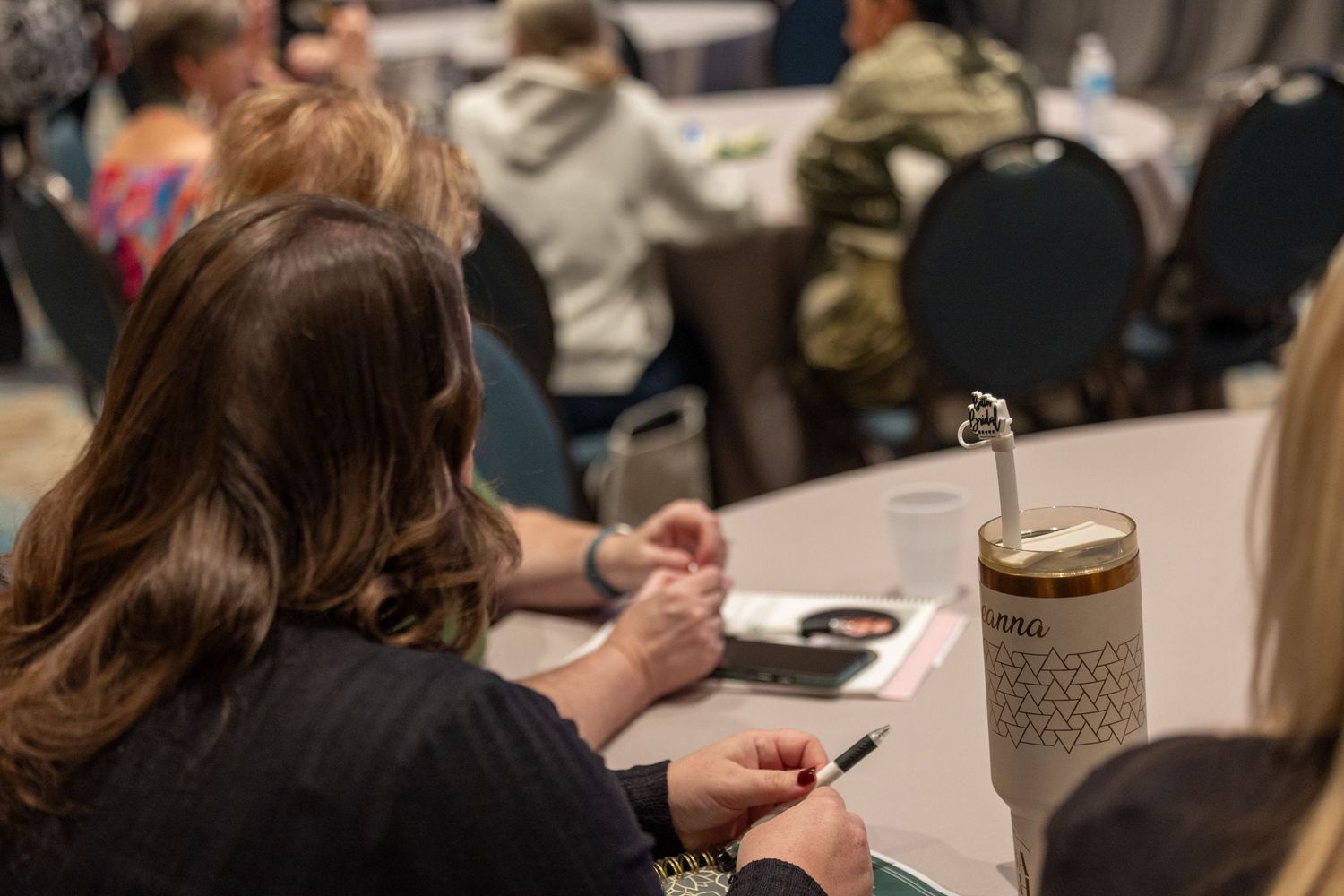 Woman taking notes with a pen at a round table during a professional conference or workshop event.