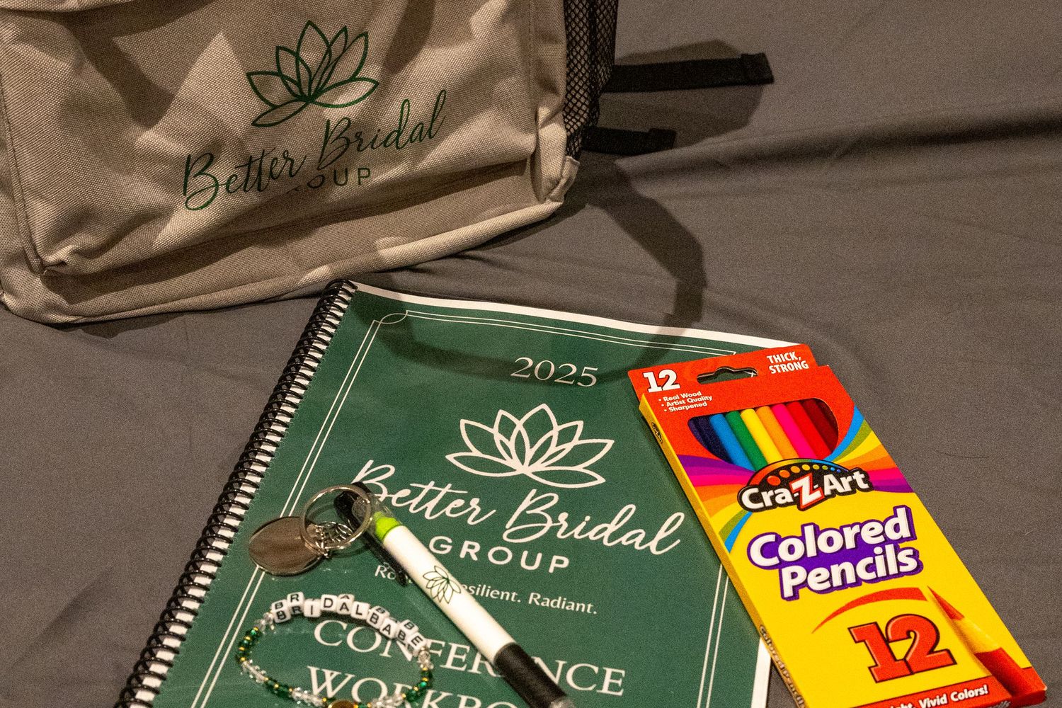 Better Bridal Group 2025 conference workbook, tote bag, colored pencils, and pen arranged on gray surface.