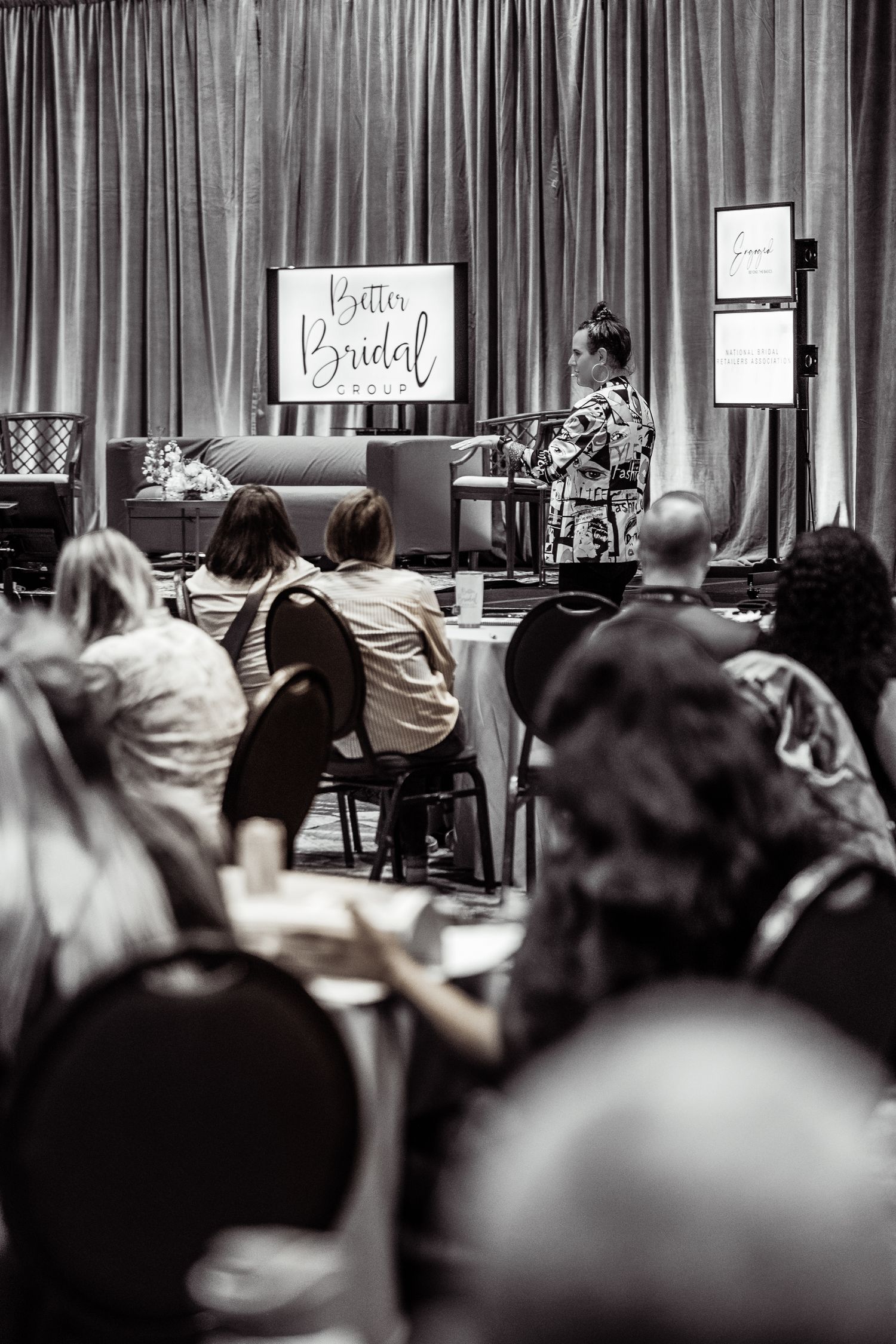 Black and white photo of attendees at Better Bridal Group seminar with speaker on stage.