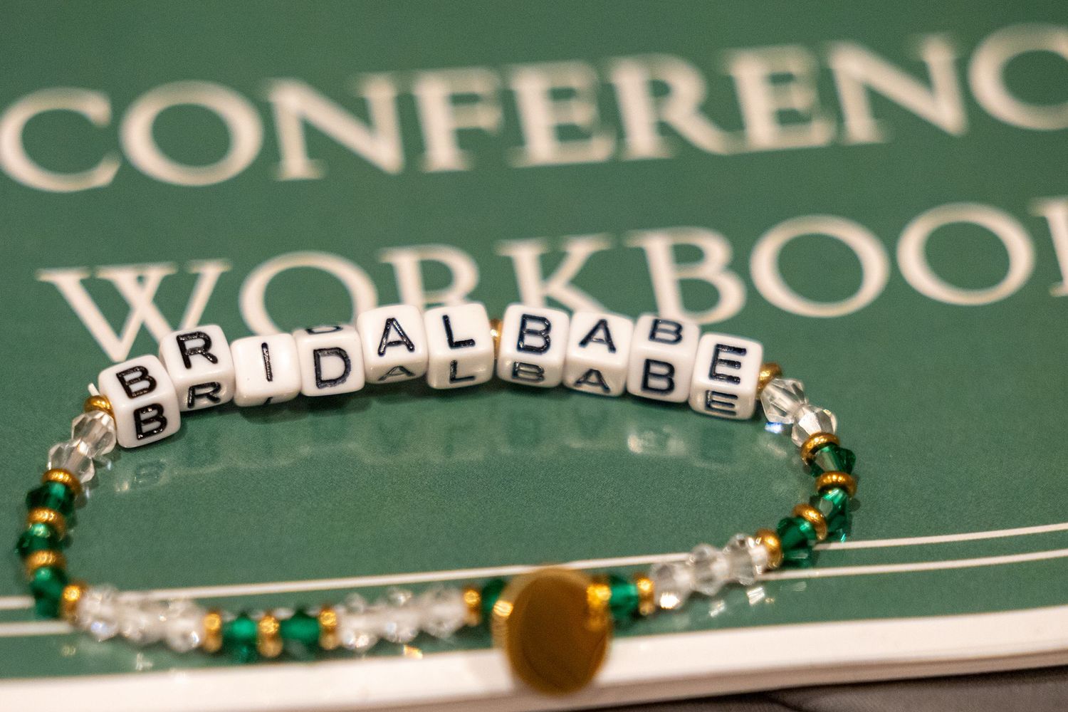 Beaded bracelet spelling BRIDALBABE resting on a Better Bridal Group conference workbook.