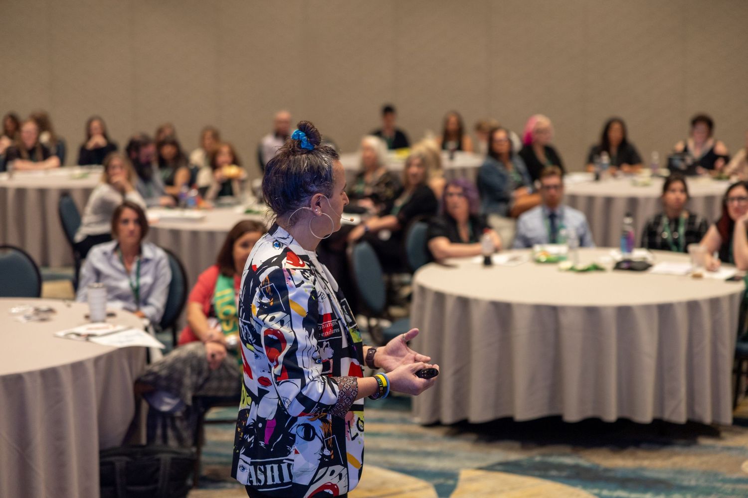 Speaker in colorful patterned outfit presenting to a large audience at a conference banquet hall.