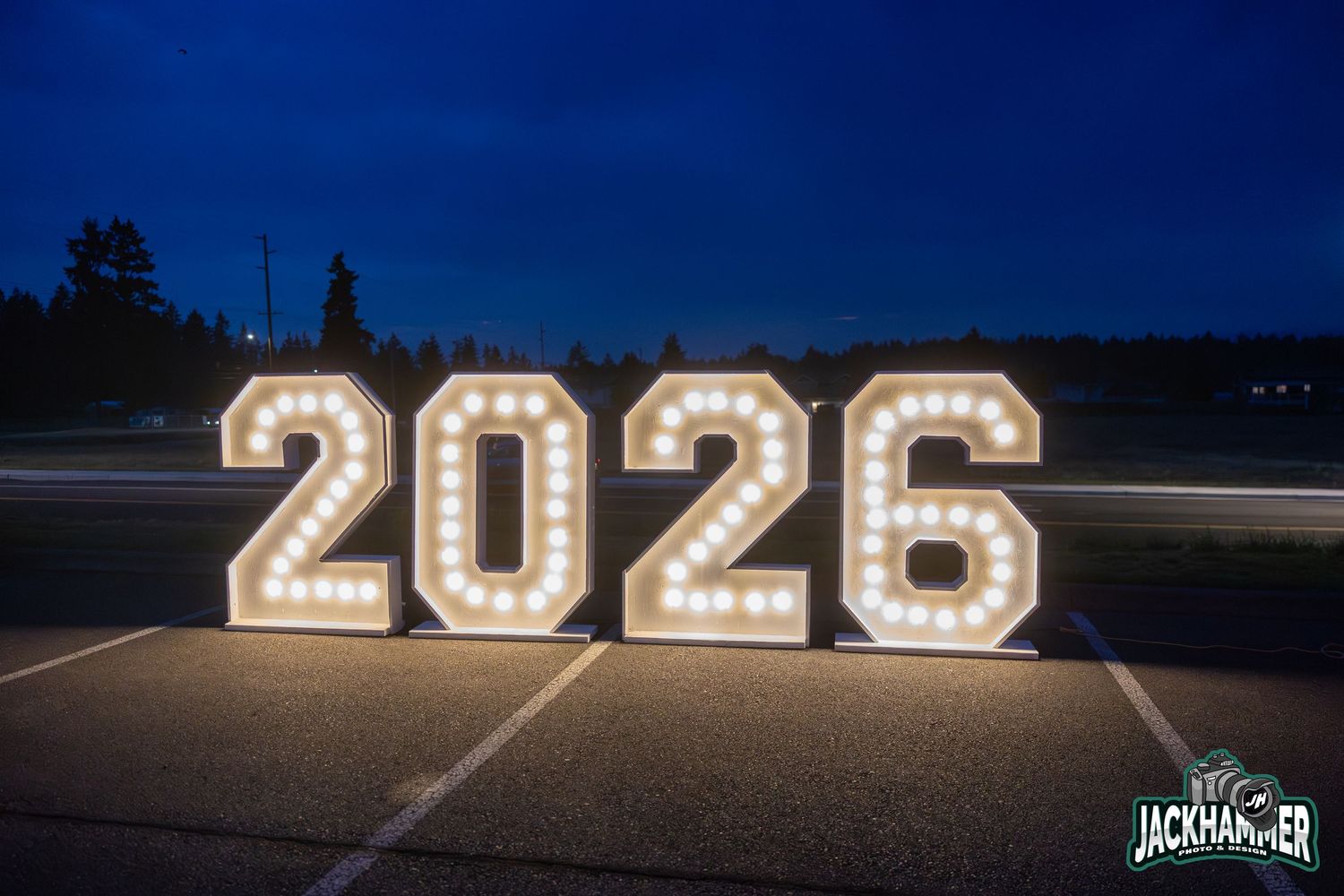 Illuminated marquee light-up 2026 graduation numbers sign displayed on pavement at night.
