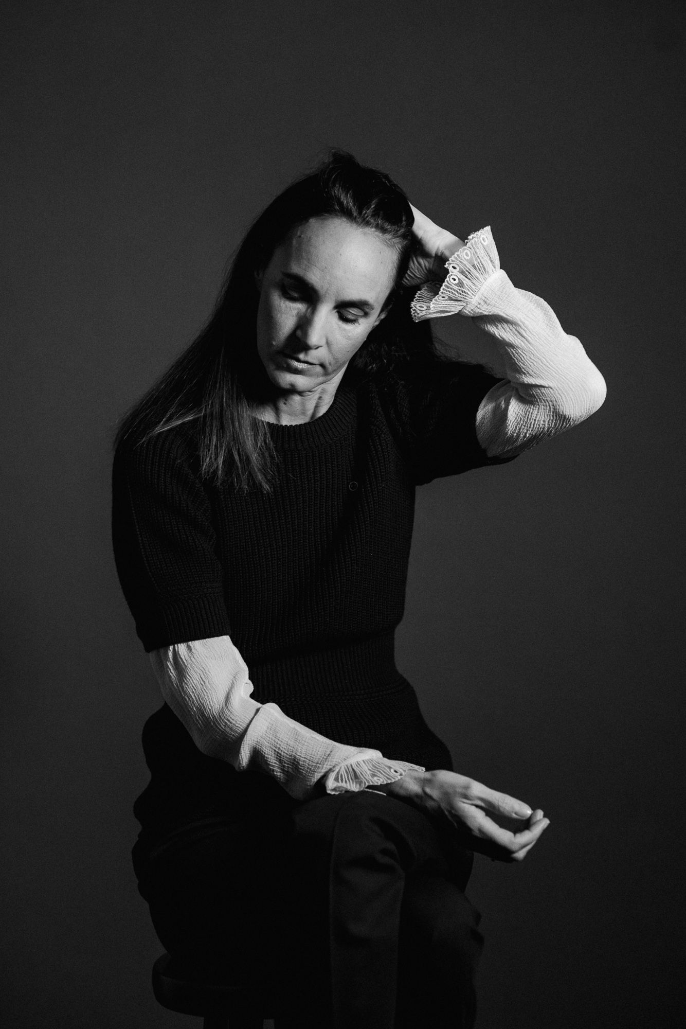 Dramatic black and white portrait of person in dark sweater making expressive hand gesture.