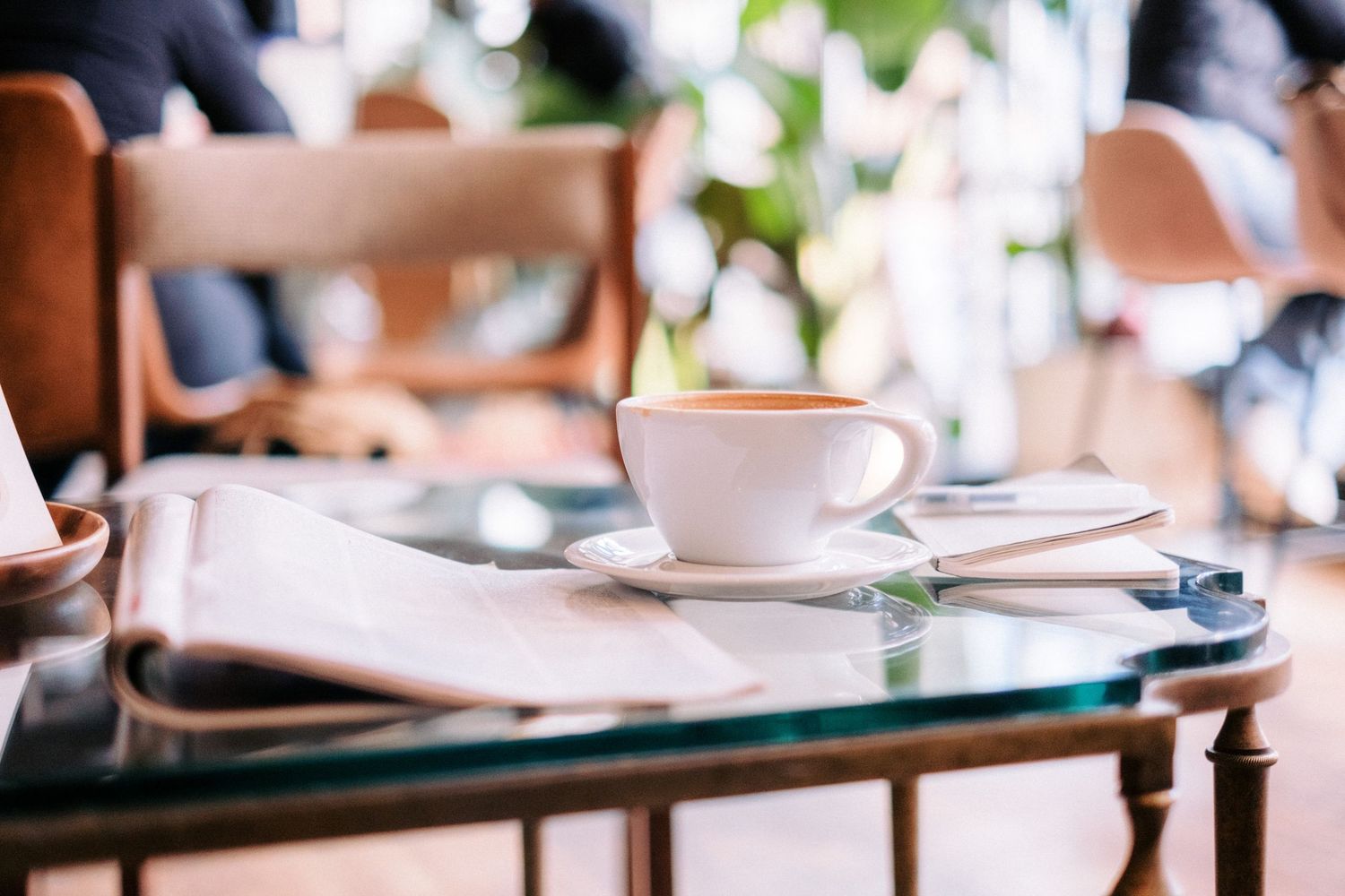 Coffee cup and reading materials arranged on wooden table in cafe setting.