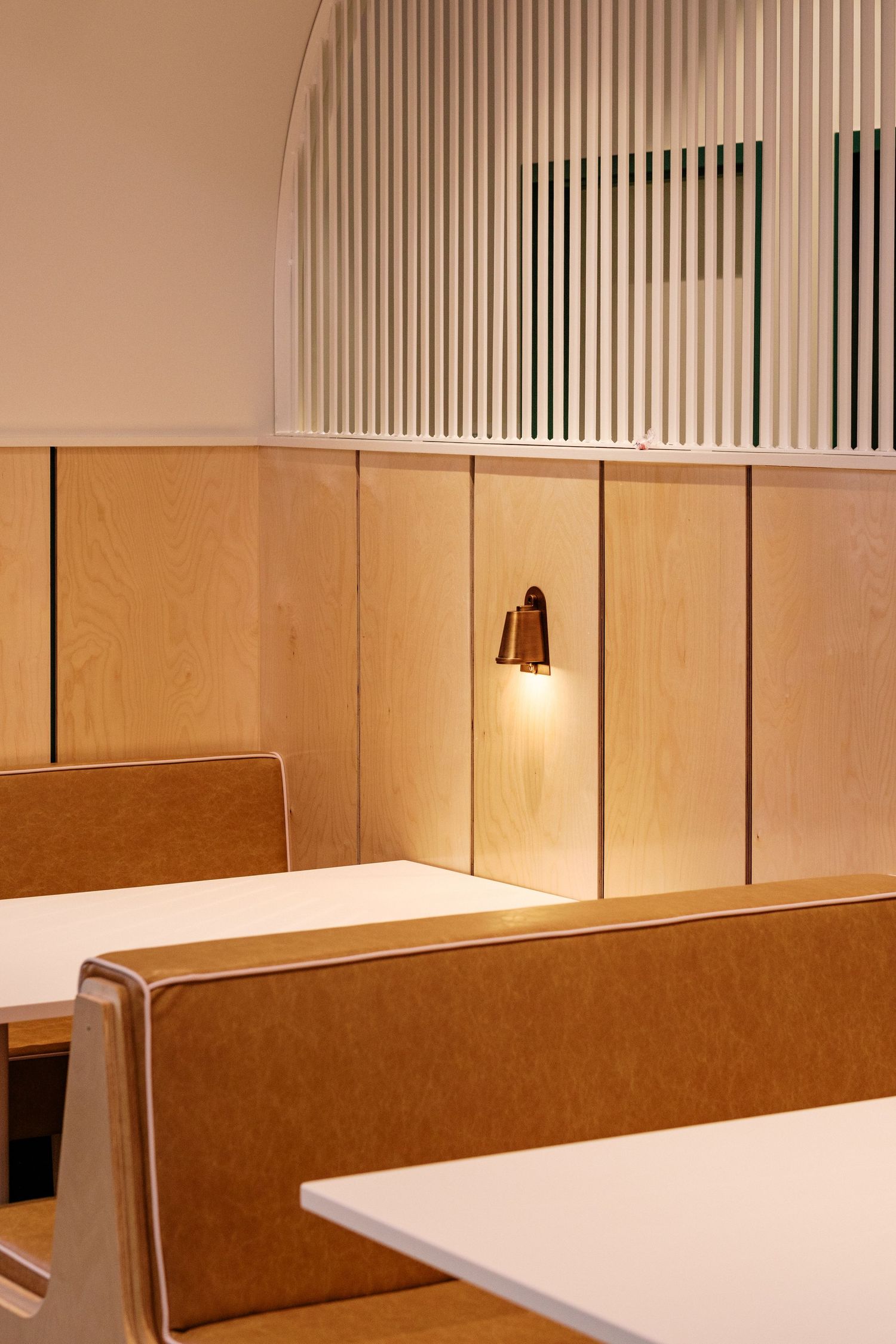 Minimalist dining area with tan booth seating, white tables, and slatted wall details.
