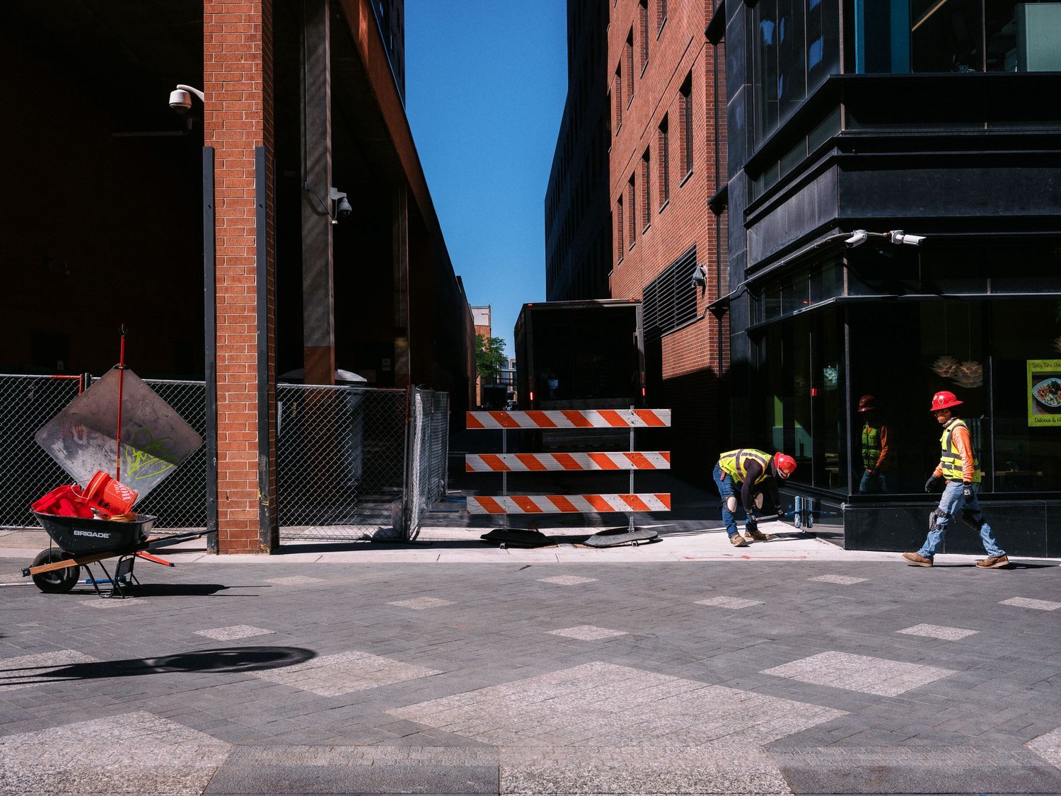 Urban street photography showing pedestrians and construction barriers in harsh sunlight.