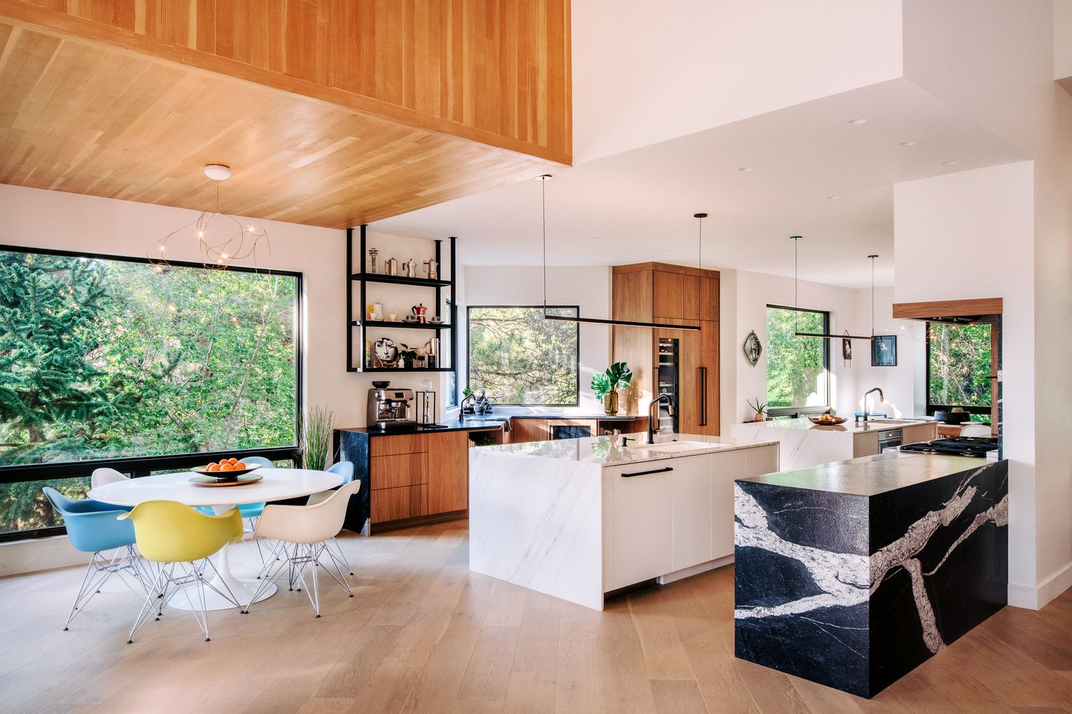 Bright modern kitchen with wood ceiling, white counters and colorful dining chairs.
