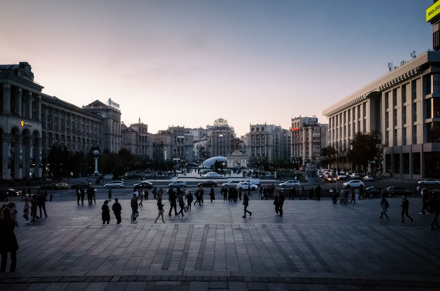 Urban plaza in evening light with historic buildings and people walking in Kiev, Ukraine.