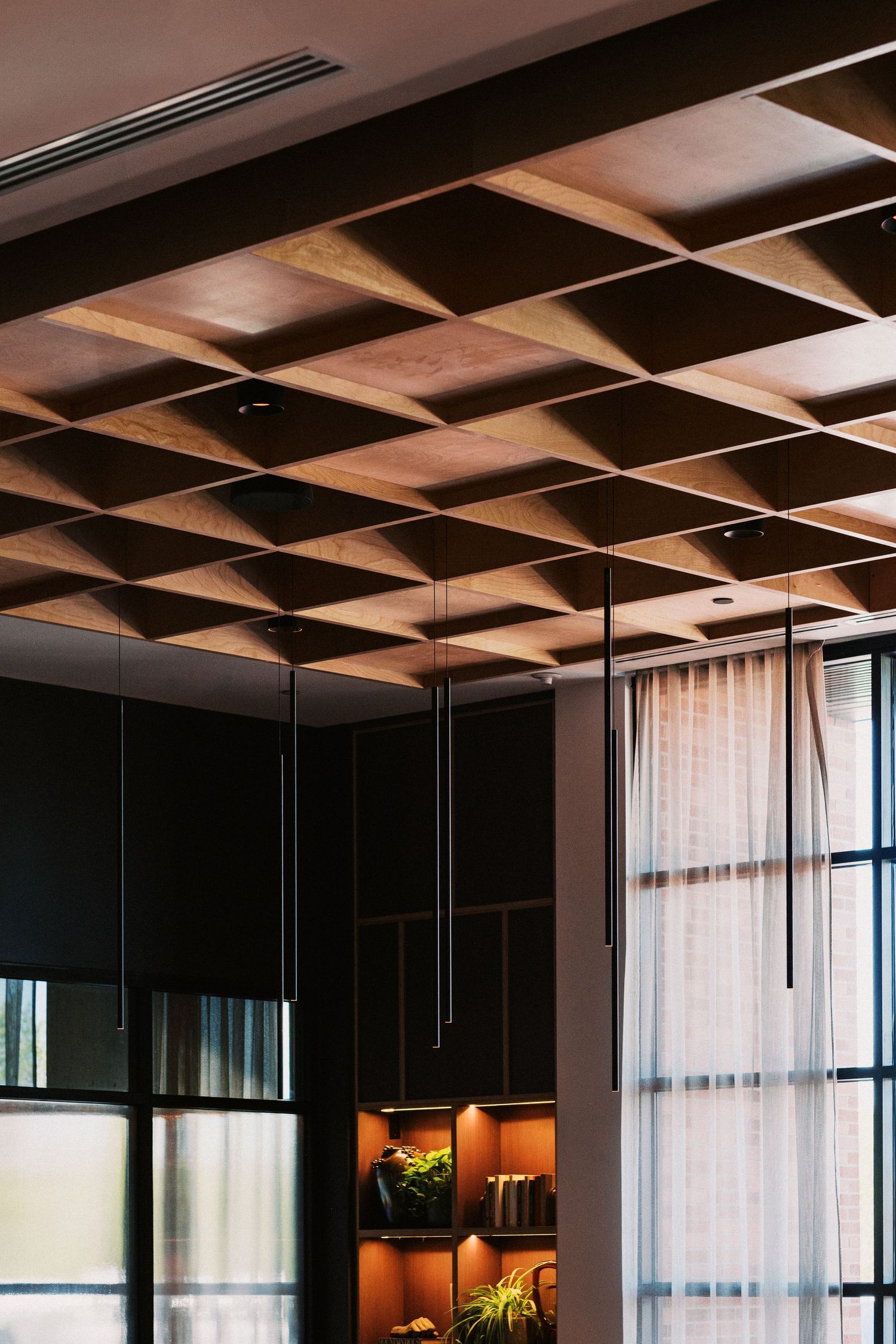Architectural detail of modern ceiling with geometric wood panels and hanging lights.