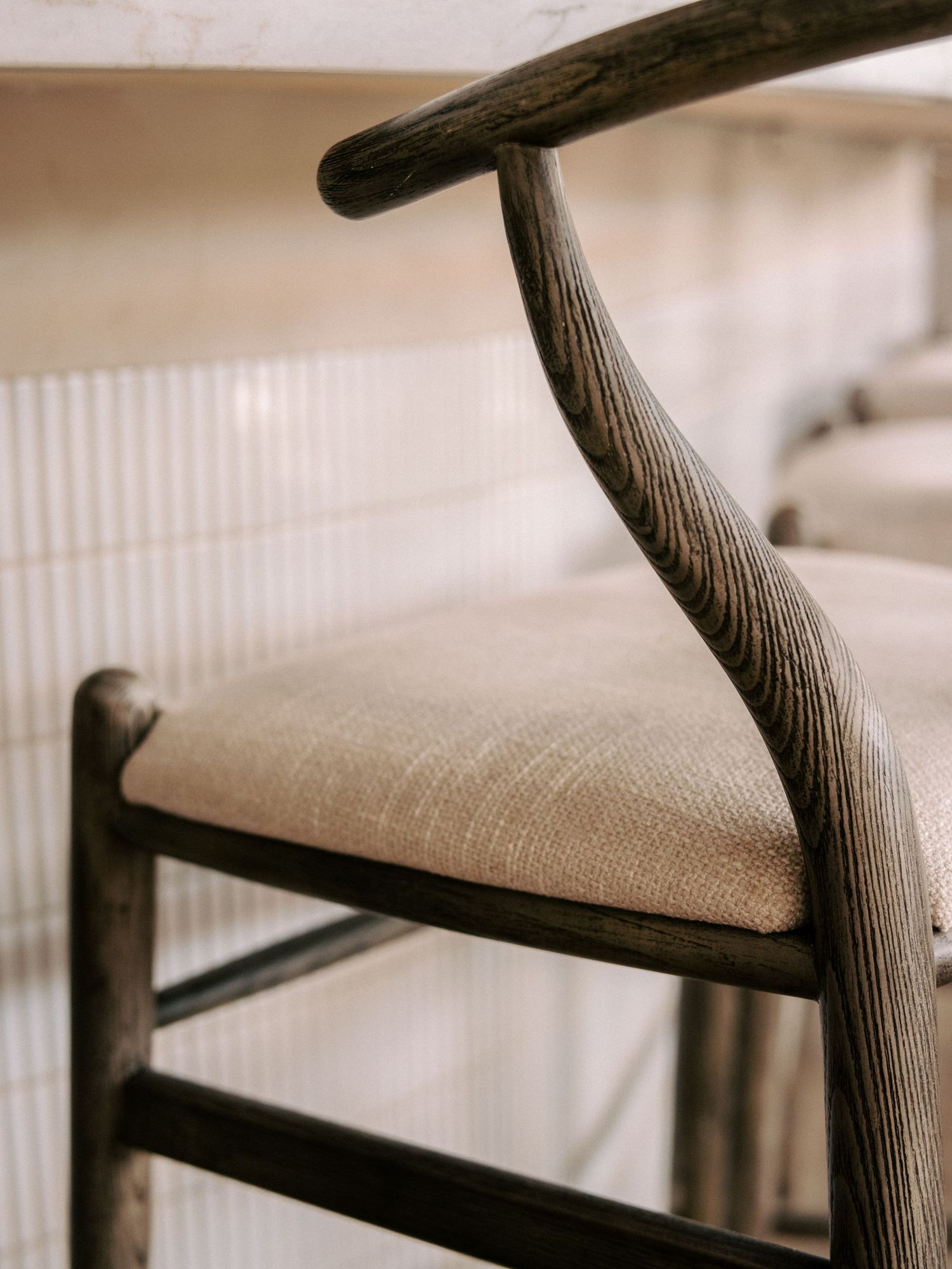 Close-up detail of wooden chair arm with textured upholstery in neutral tones.