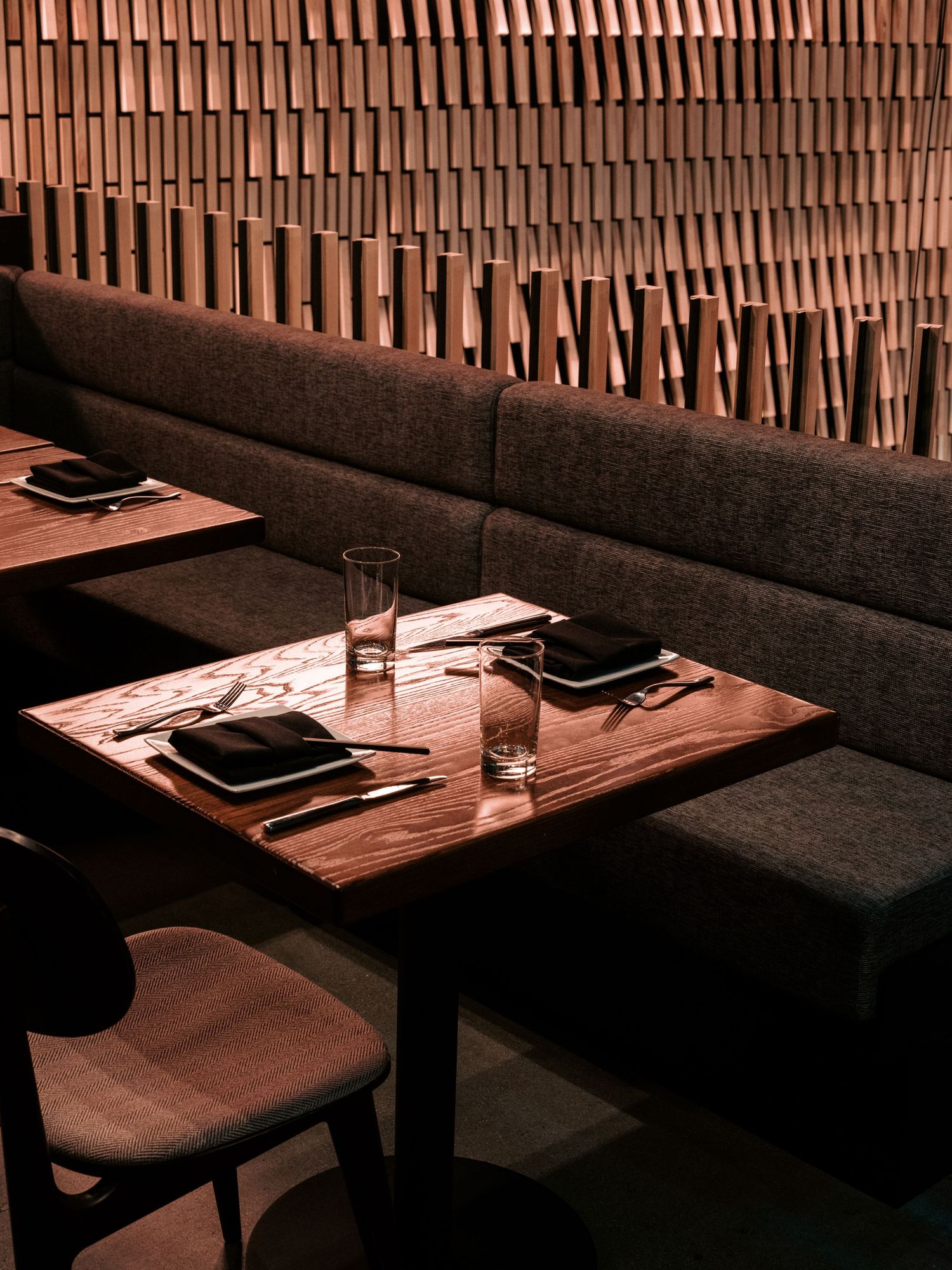 Intimate dining setup with wooden table and bench seating against textured wall paneling.