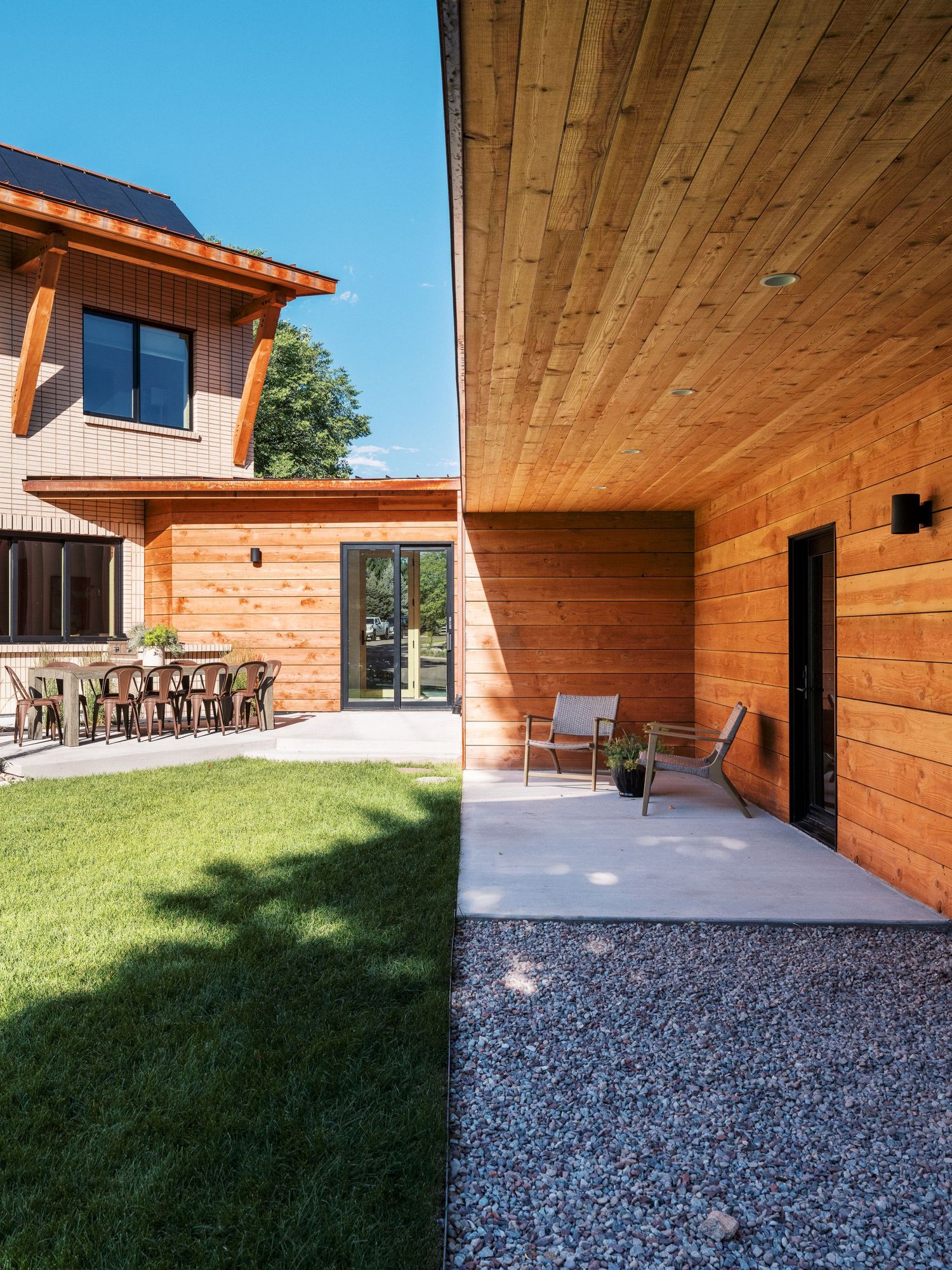 Covered outdoor patio area with gravel ground and wooden ceiling extending from modern house.