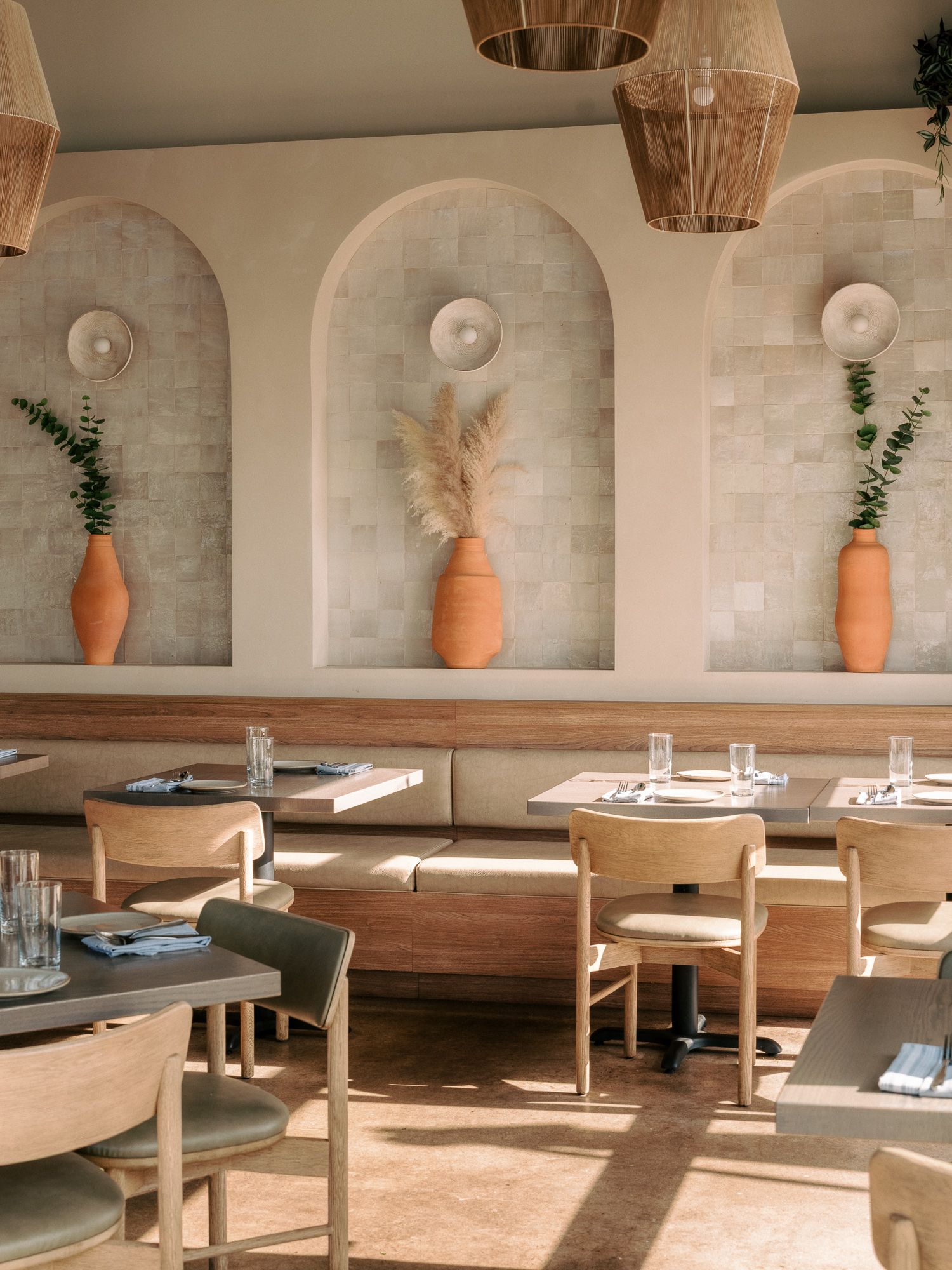 Modern restaurant interior with arched alcoves, terracotta vases and minimalist furniture.