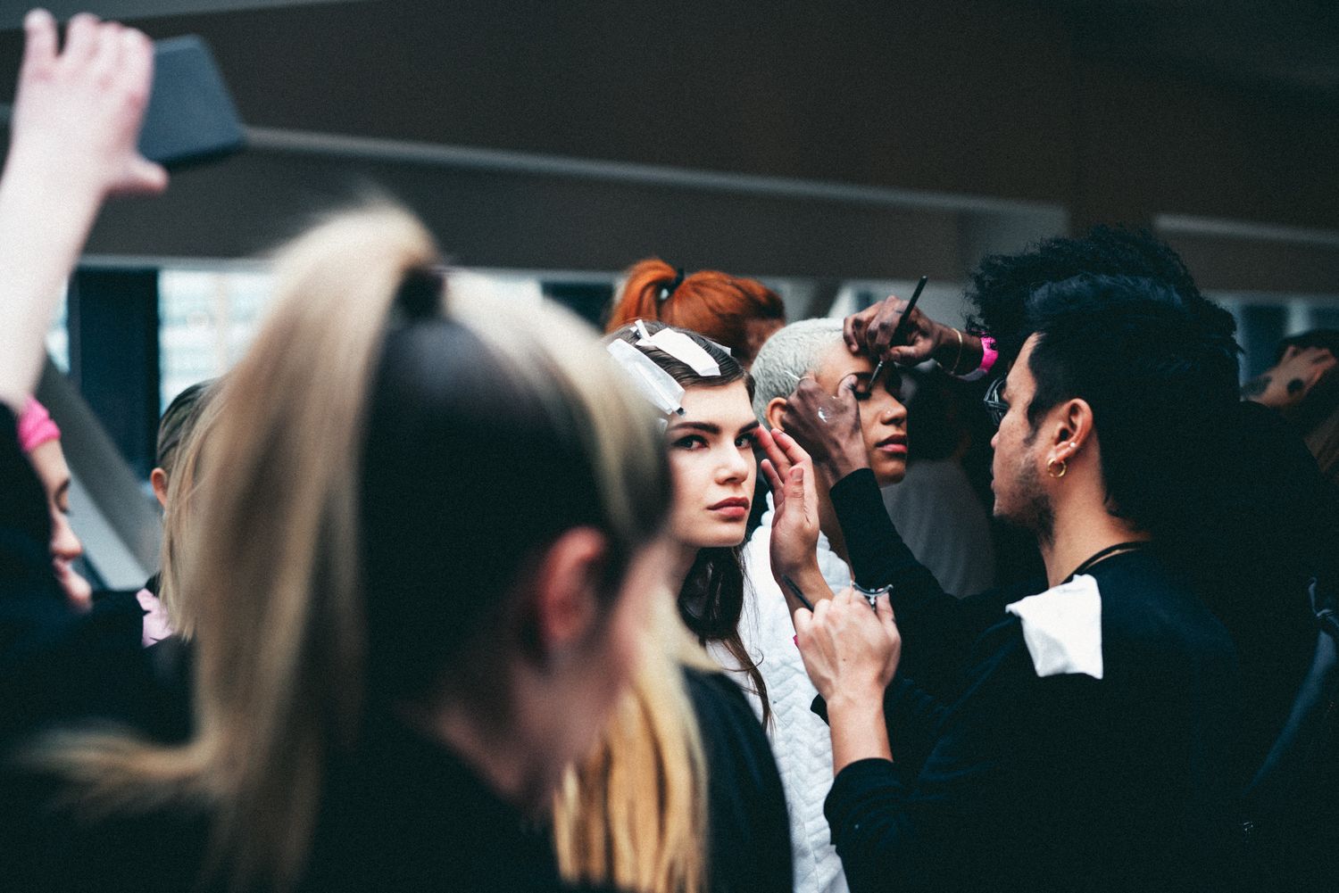 Models and stylists backstage at a fashion show, with dramatic hair and makeup preparations underway.