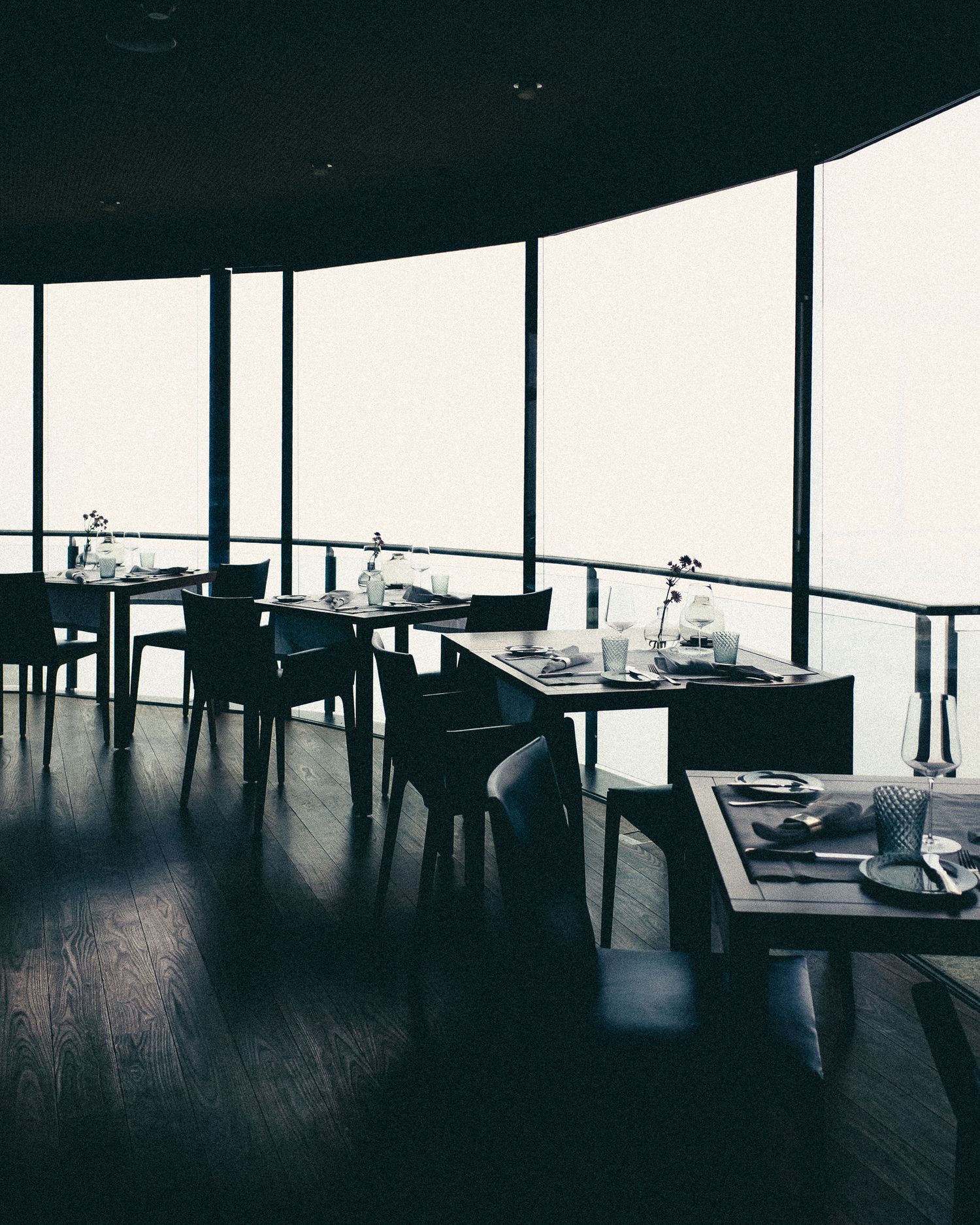 Modern restaurant interior with dark wood floors and floor-to-ceiling windows offering panoramic views.