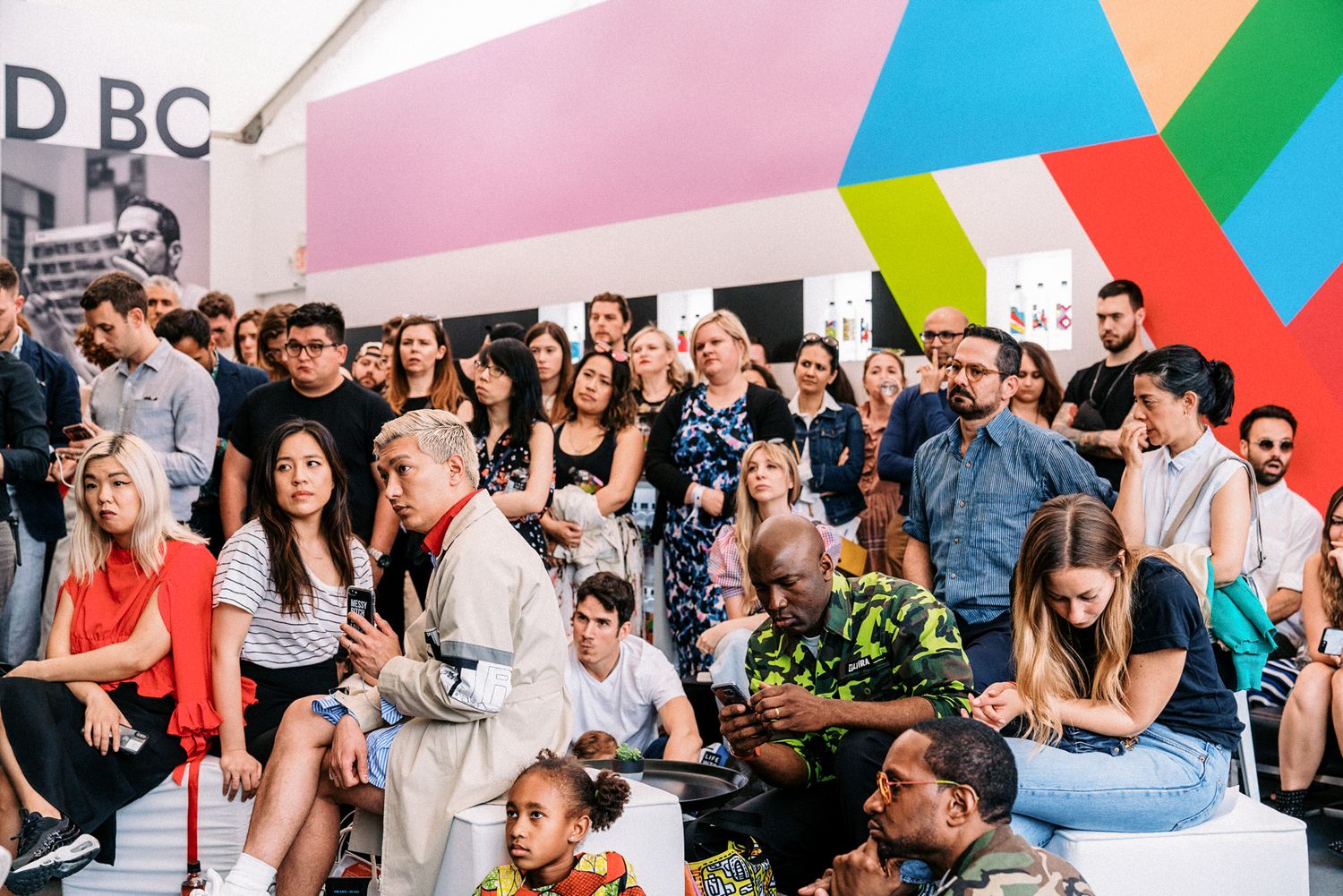 Diverse crowd of people gathered at a colorful art fair event with geometric murals in the background.