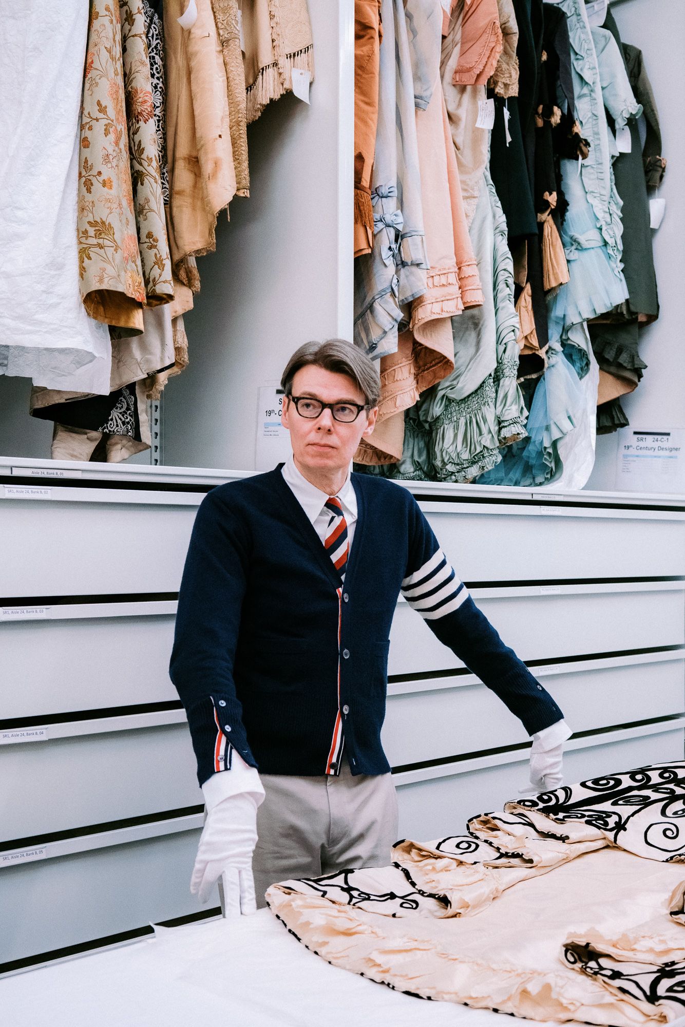 Person in cardigan and tie standing in front of rack of vintage clothing.