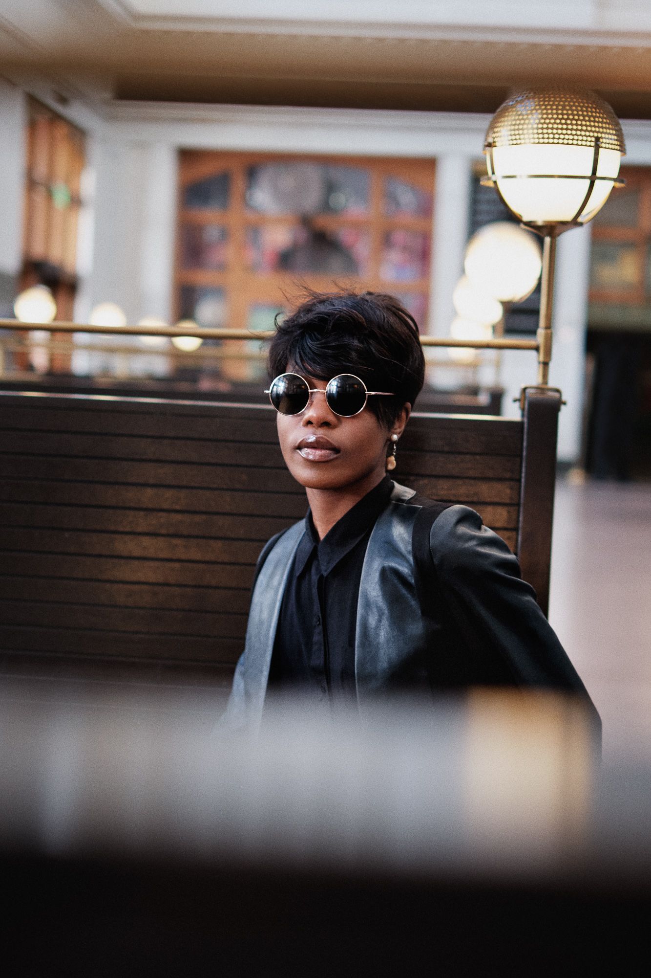 Stylish portrait with round sunglasses and leather jacket in indoor setting with decorative lighting.