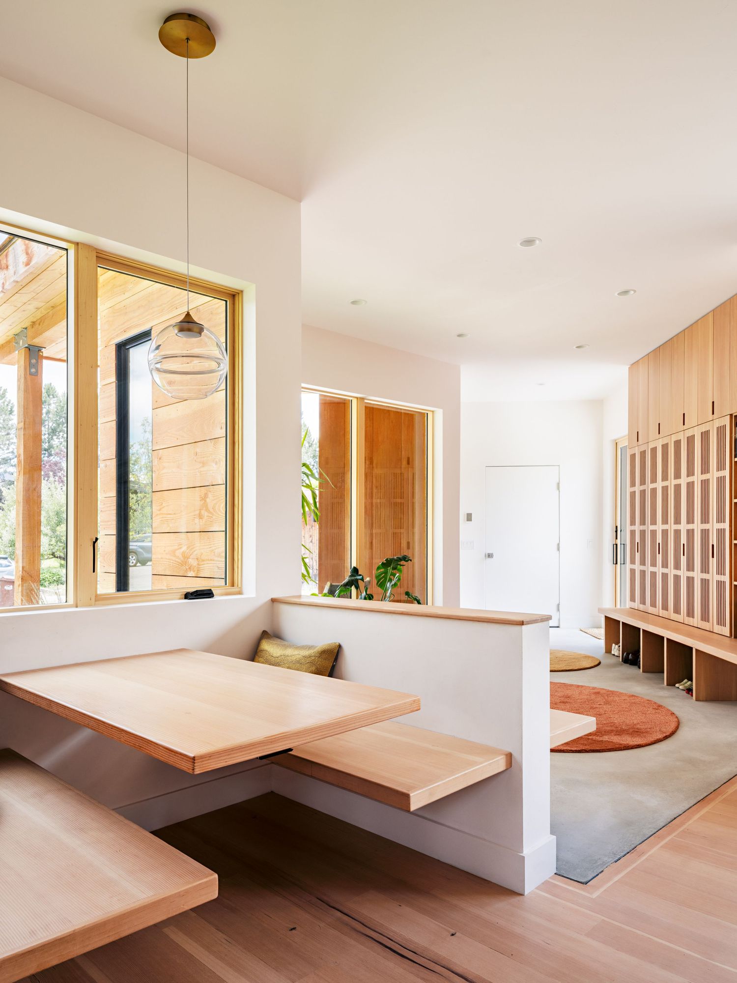 Minimalist interior space with wooden built-in furniture and large windows letting in natural light.