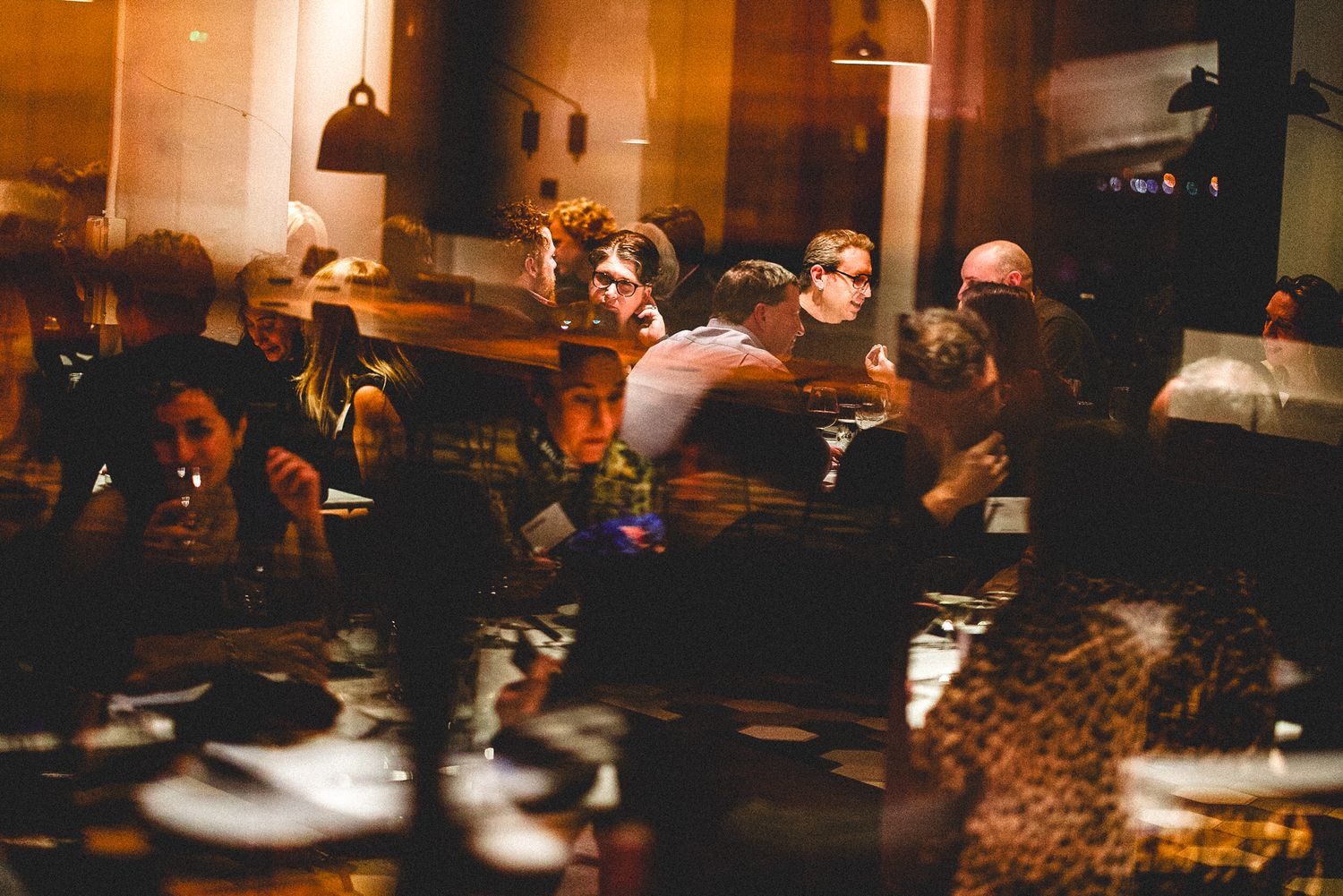 Crowd of people socializing in a warmly lit restaurant during a busy evening gathering.