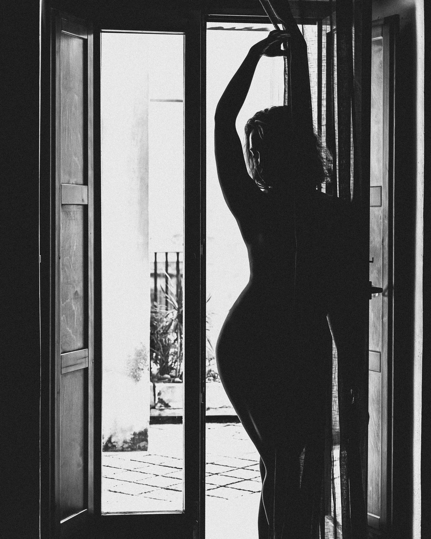 A silhouetted figure stretches in a doorway against bright light, creating a dramatic black and white composition.