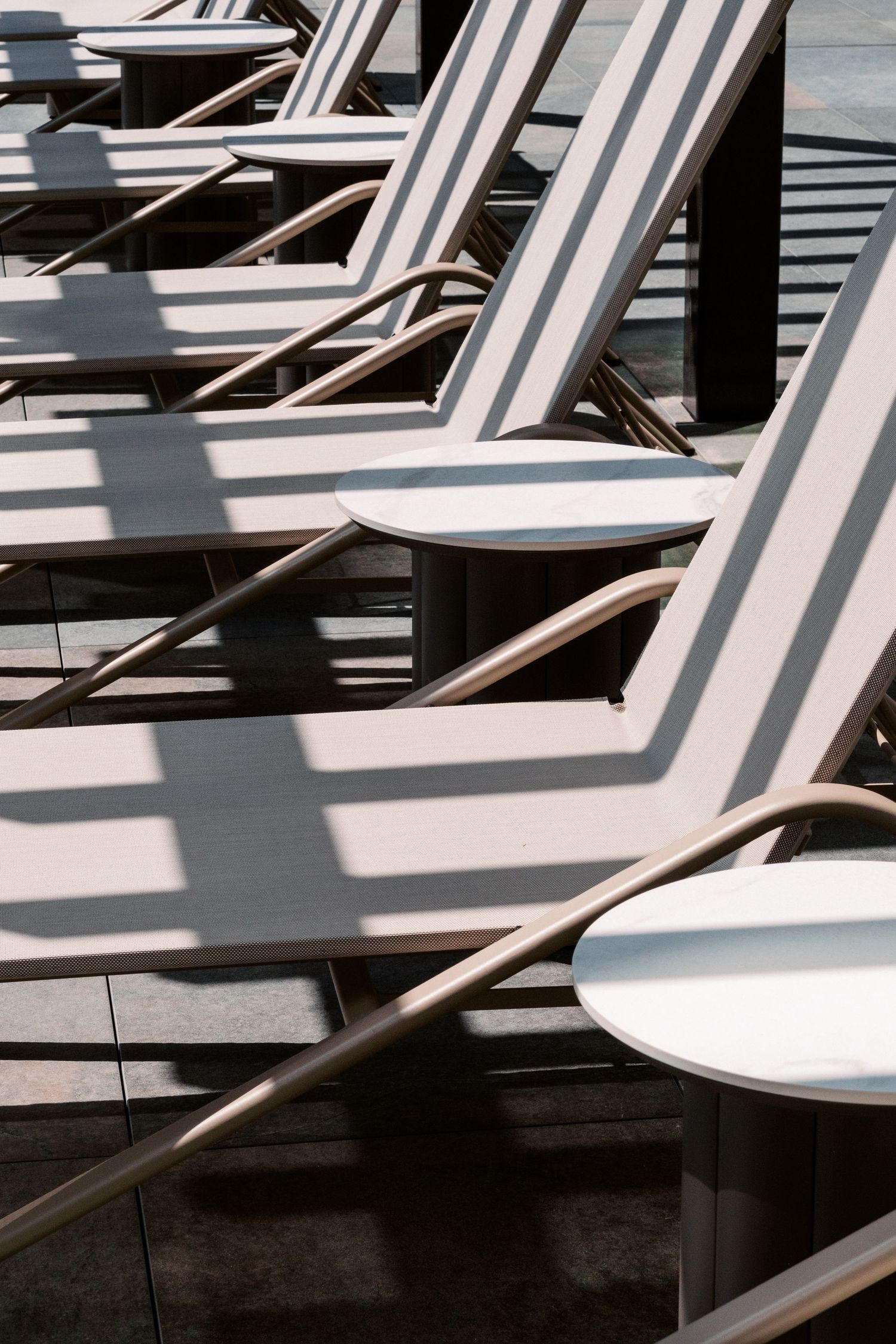 Row of white lounge chairs creating geometric shadows in bright sunlight.