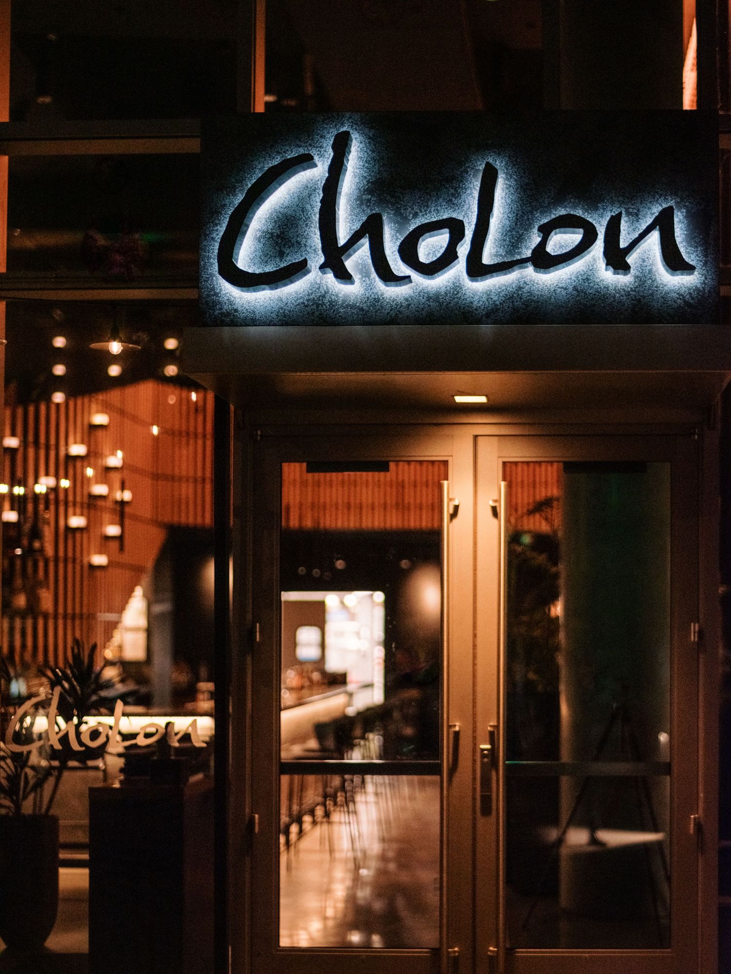 Illuminated Cholon restaurant sign above entrance with wooden slat wall decor.