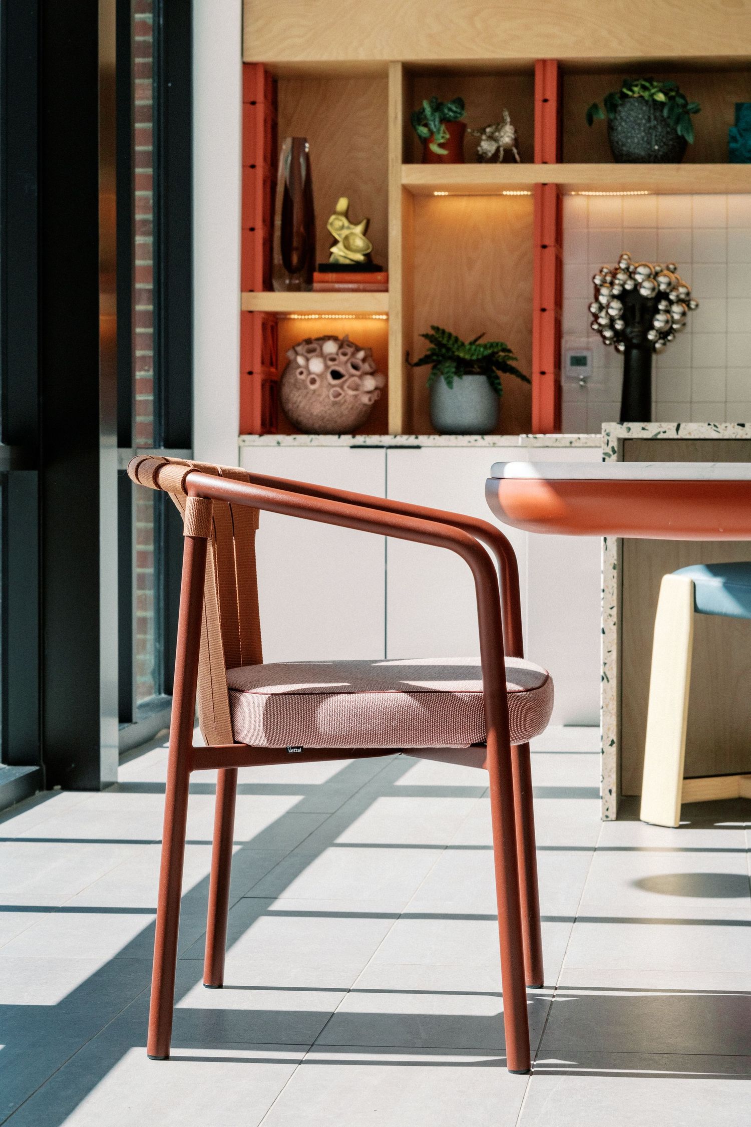 Stylish wooden dining chair with pink cushion against built-in shelving display.
