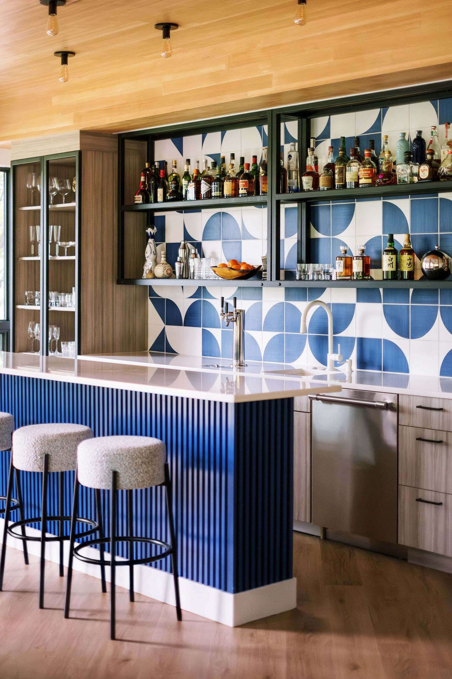 Stylish home bar with blue geometric backsplash tiles and gray upholstered bar stools.