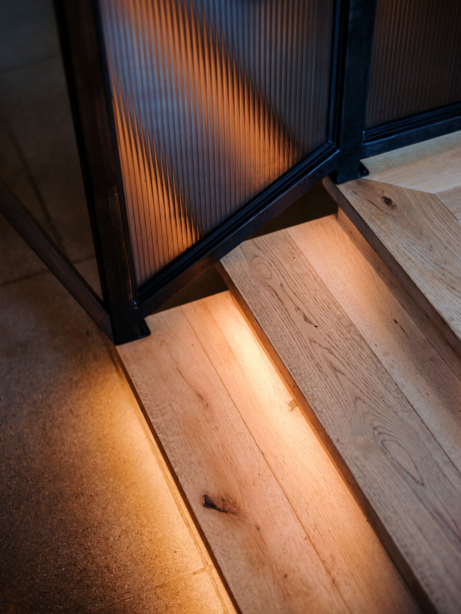Warm light streaming through black frame onto wooden flooring creates dramatic shadows.