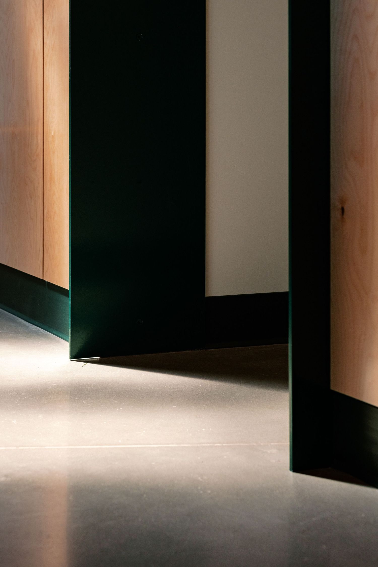 Dramatic lighting creates shadows through wooden doorways in a minimalist corridor.