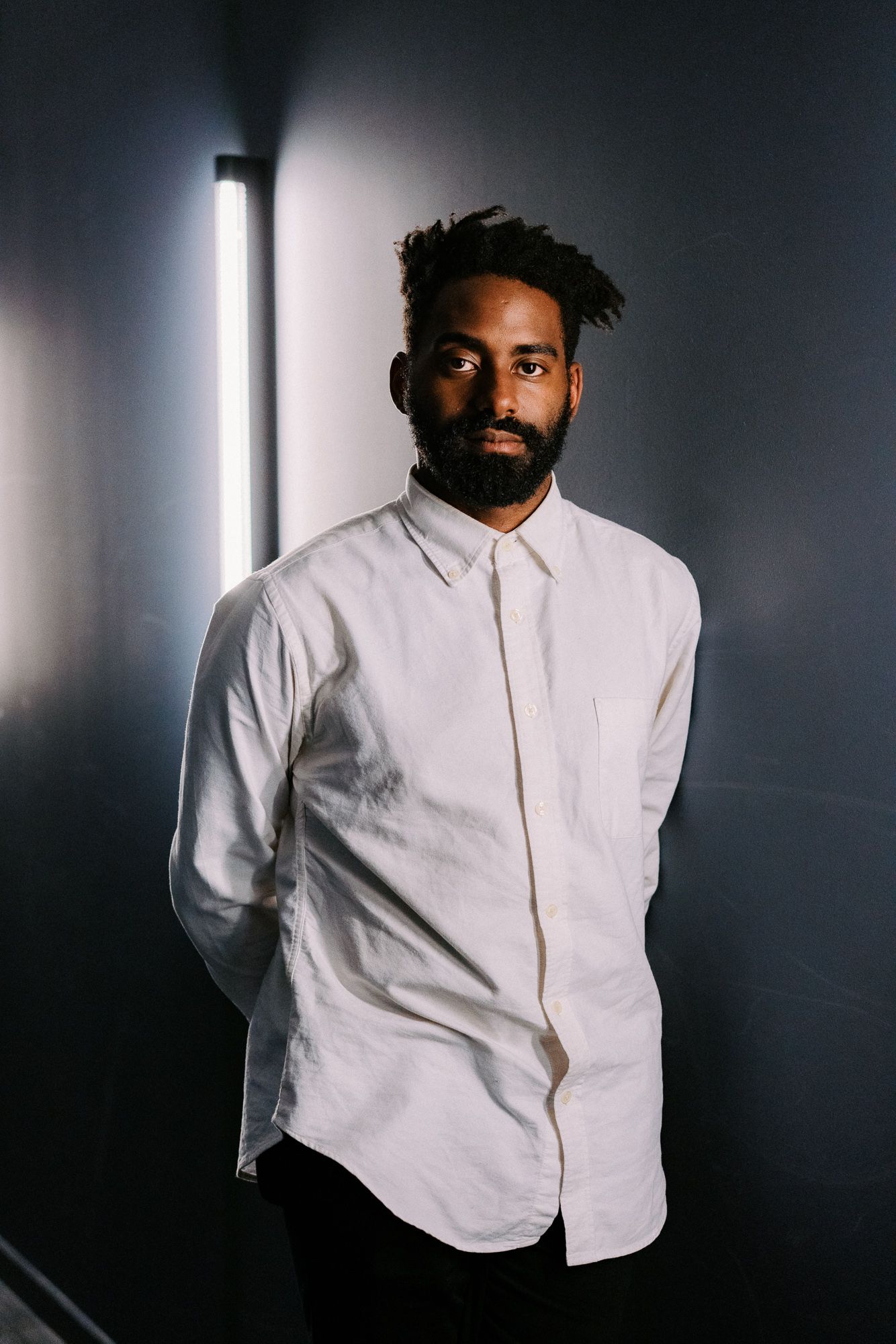Portrait of person in white button-down shirt against dark background with dramatic side lighting.