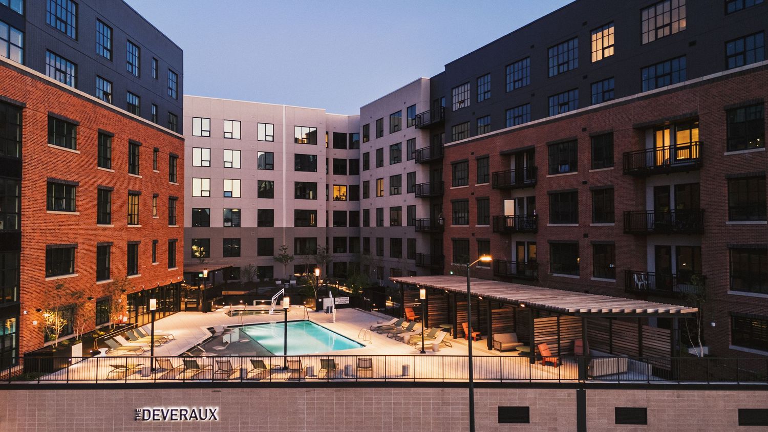 Multi-story residential buildings with illuminated windows and parking area in evening light.