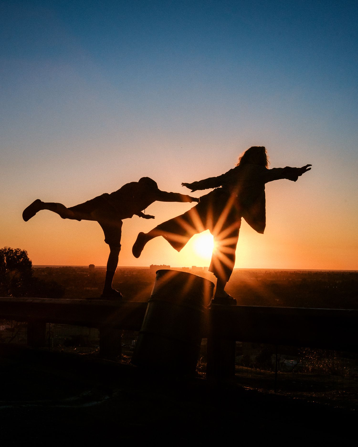 Silhouettes of dancers performing dynamic moves against a golden sunset sky.