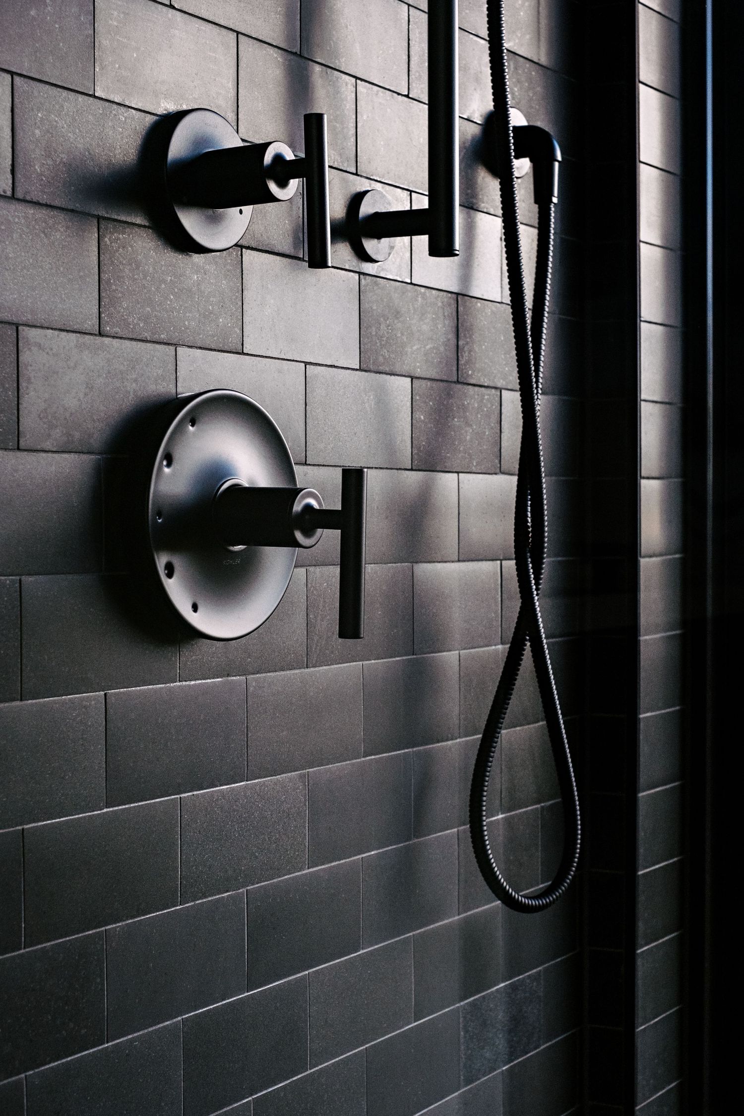Dramatic black tiled shower wall with modern matte black fixtures and shower heads.