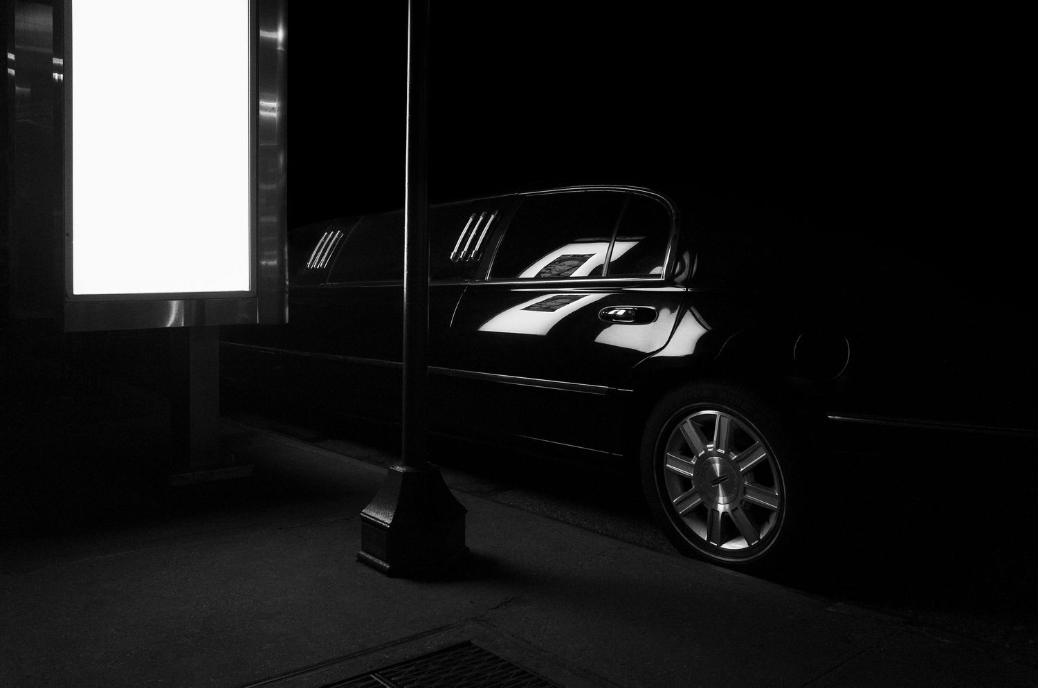 A black luxury car parked in dark shadows with chrome wheels reflecting minimal light in a moody nighttime scene.
