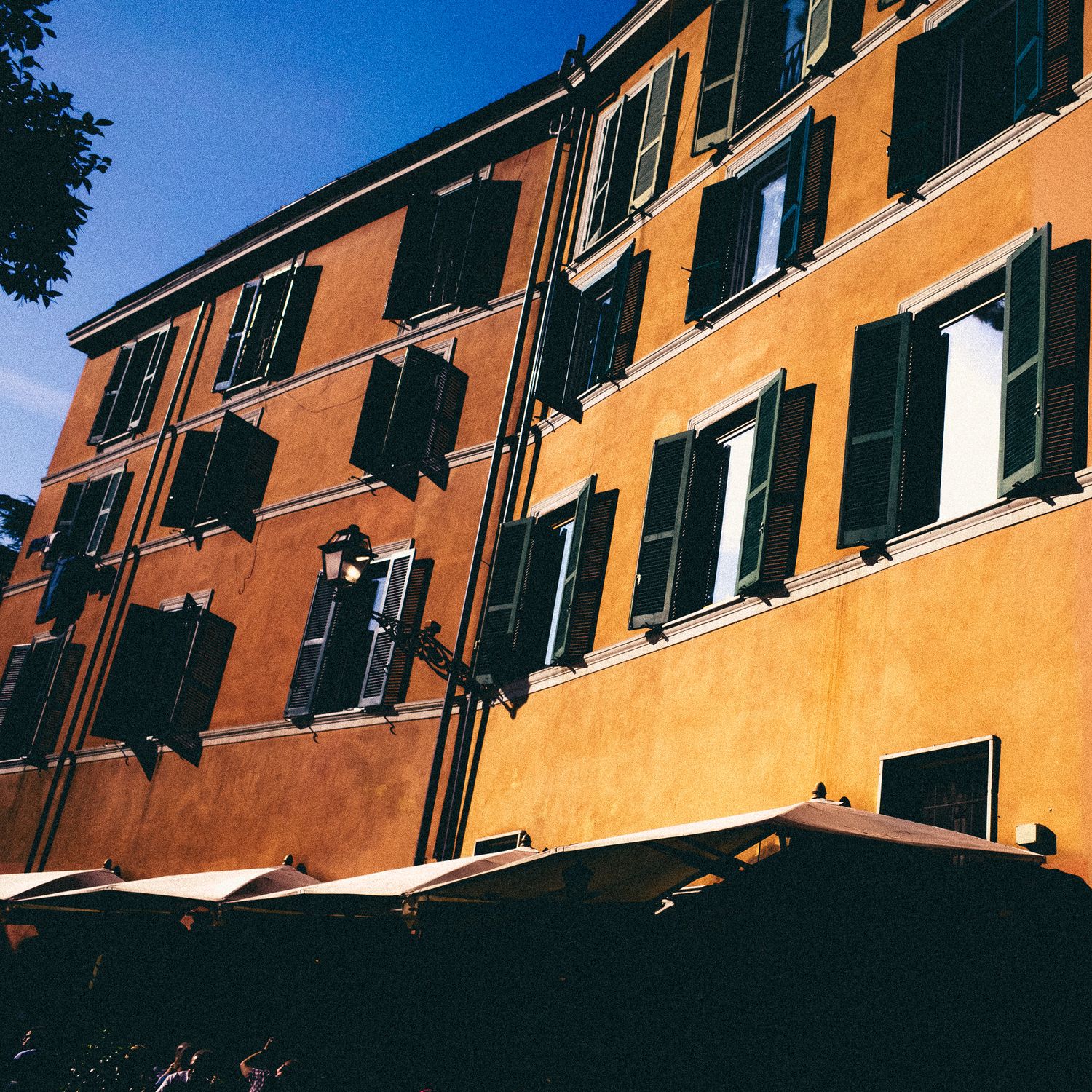 Row of orange apartment buildings with white shuttered windows photographed from a low angle against blue sky.