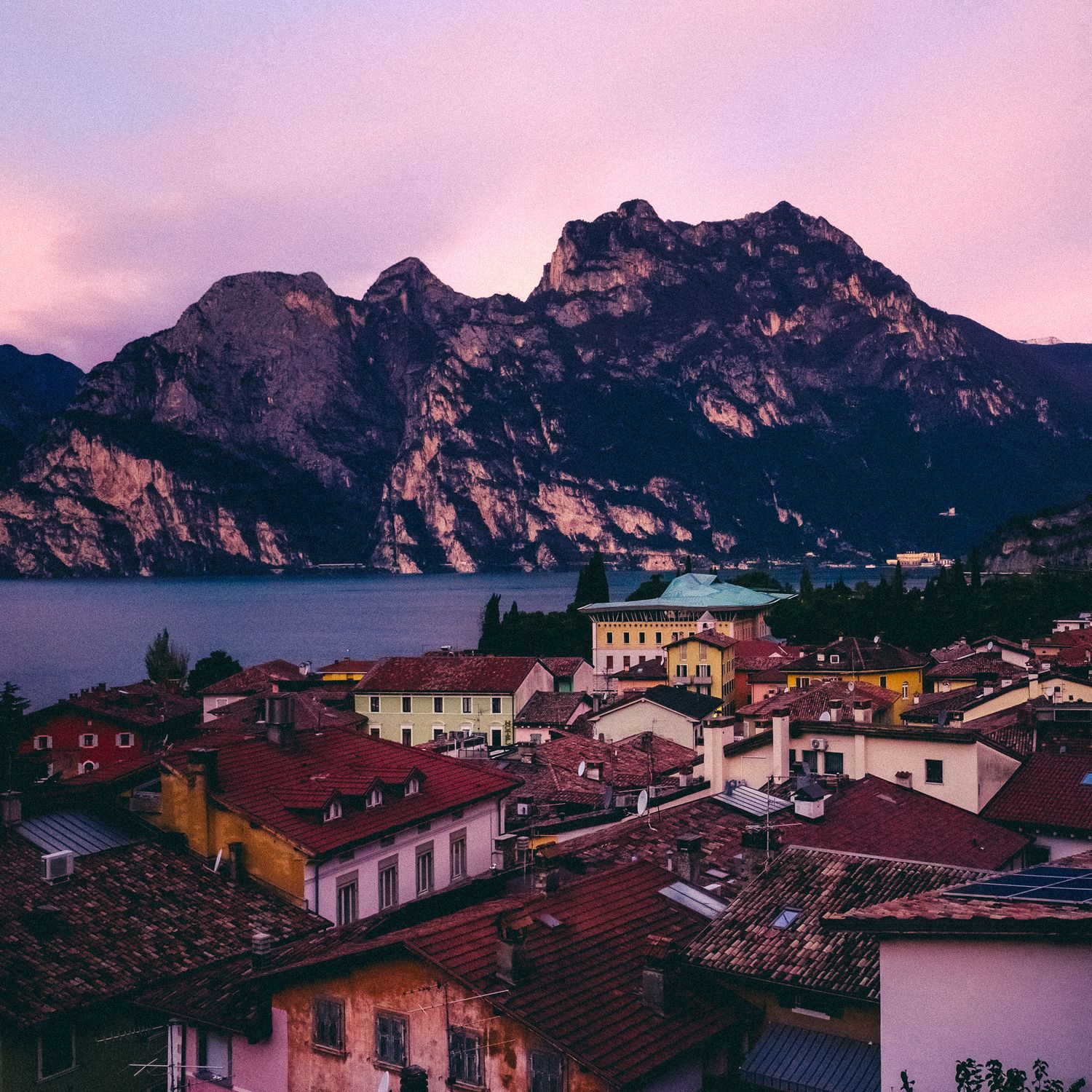 Mountain village with red-roofed buildings nestled along a lake during a pink and purple sunset.