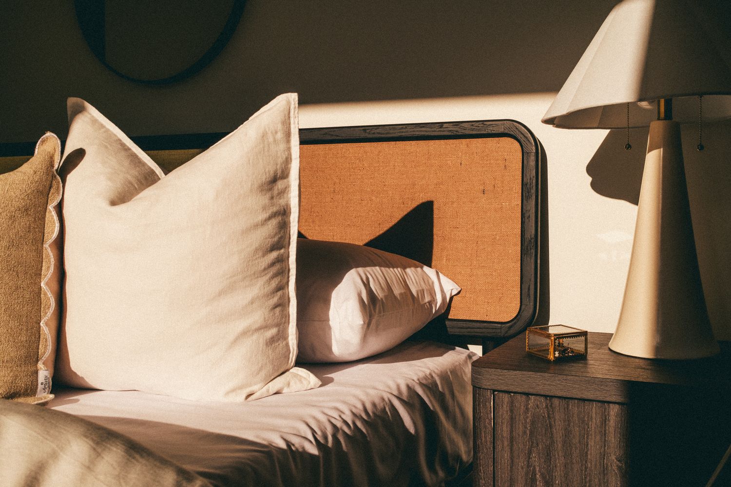 Cozy bedroom headboard with linen pillows, cane detail, and warm bedside lamp light.