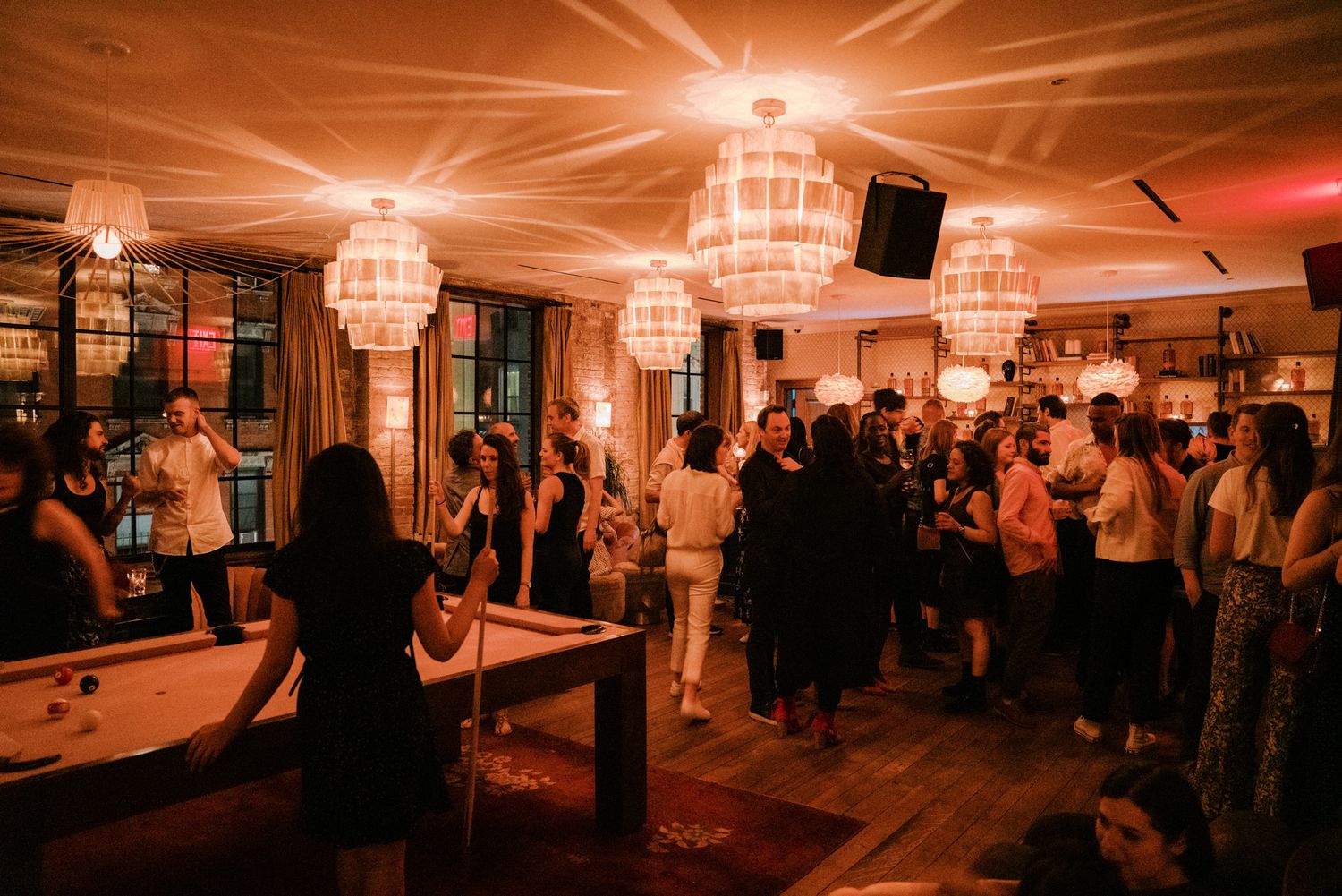 Crowded upscale bar venue with warm red lighting and elegant crystal chandeliers during a social event.