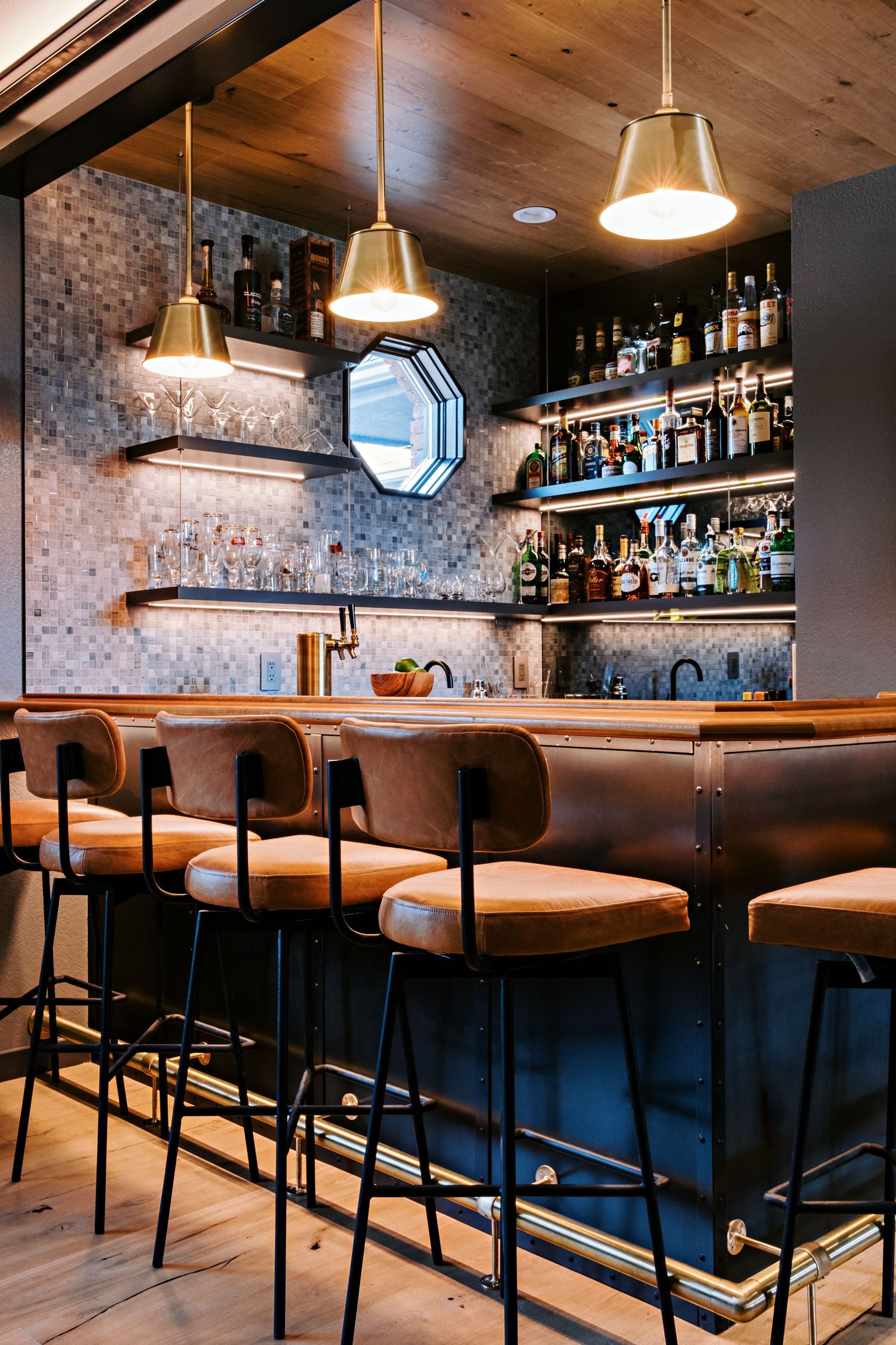 Modern bar counter with leather barstools and extensive bottle display on illuminated shelving.