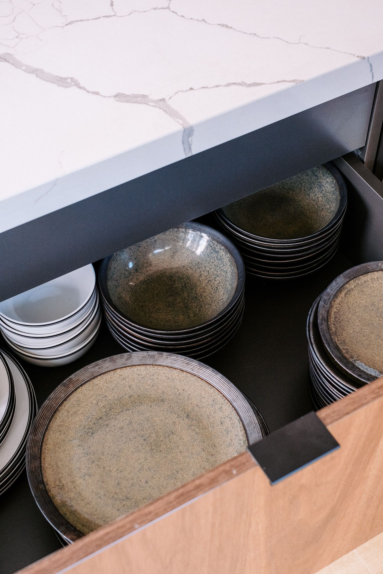 Organized drawer storage showing stacked ceramic plates in dark wood cabinetry.