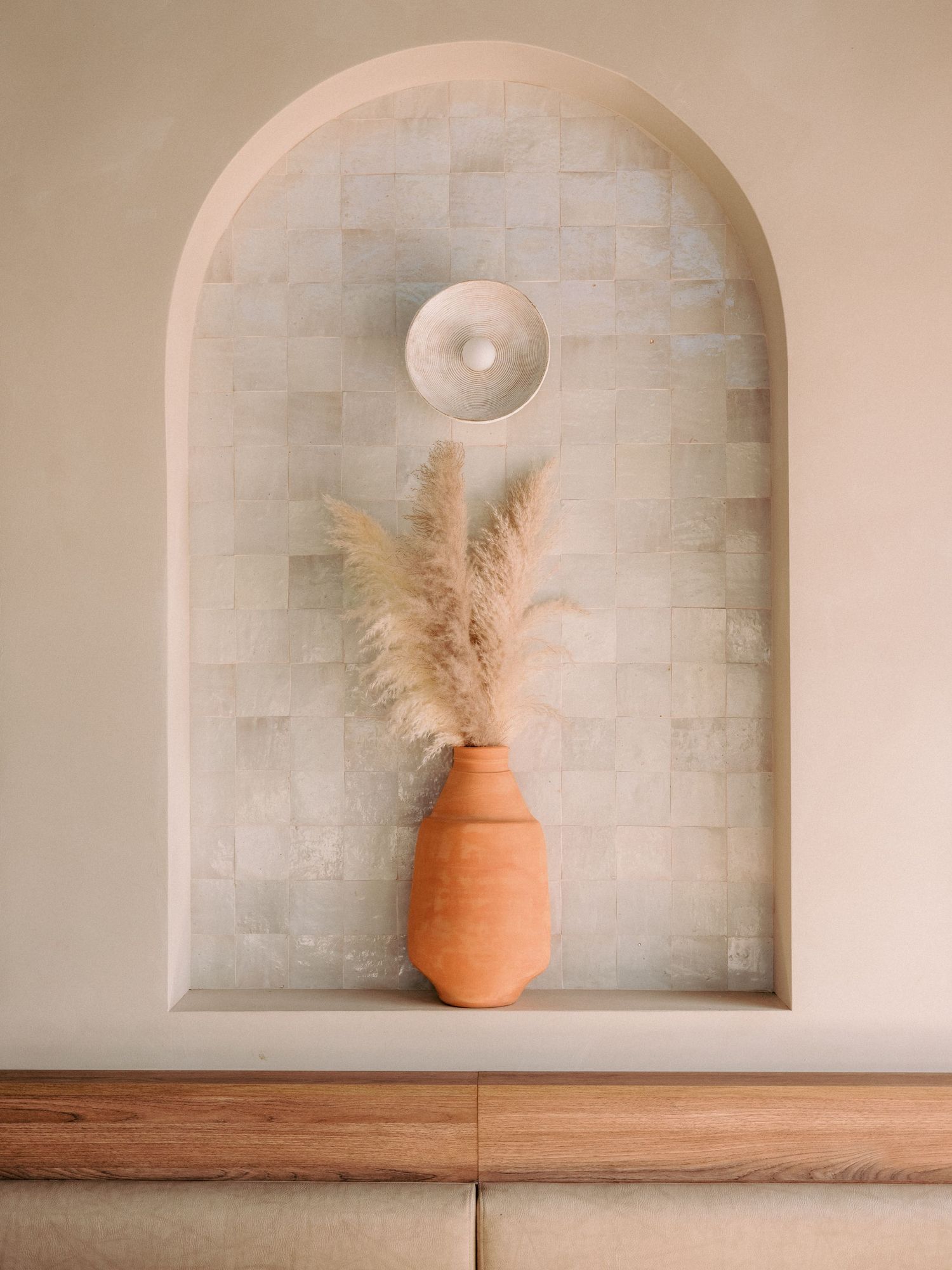 Decorative terracotta vase with dried pampas grass displayed in an arched wall niche.