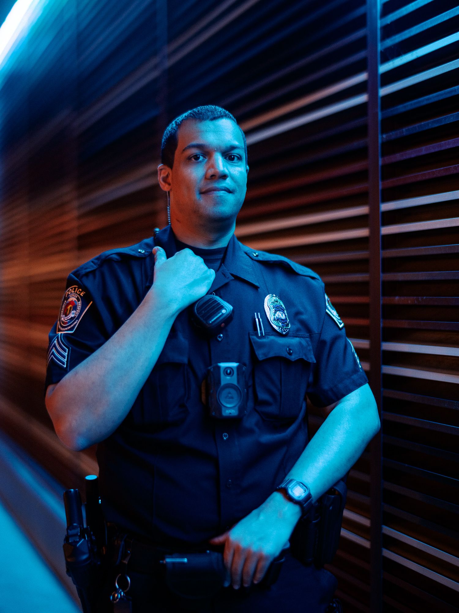 Police officer in uniform illuminated by dramatic blue lighting against dark background.