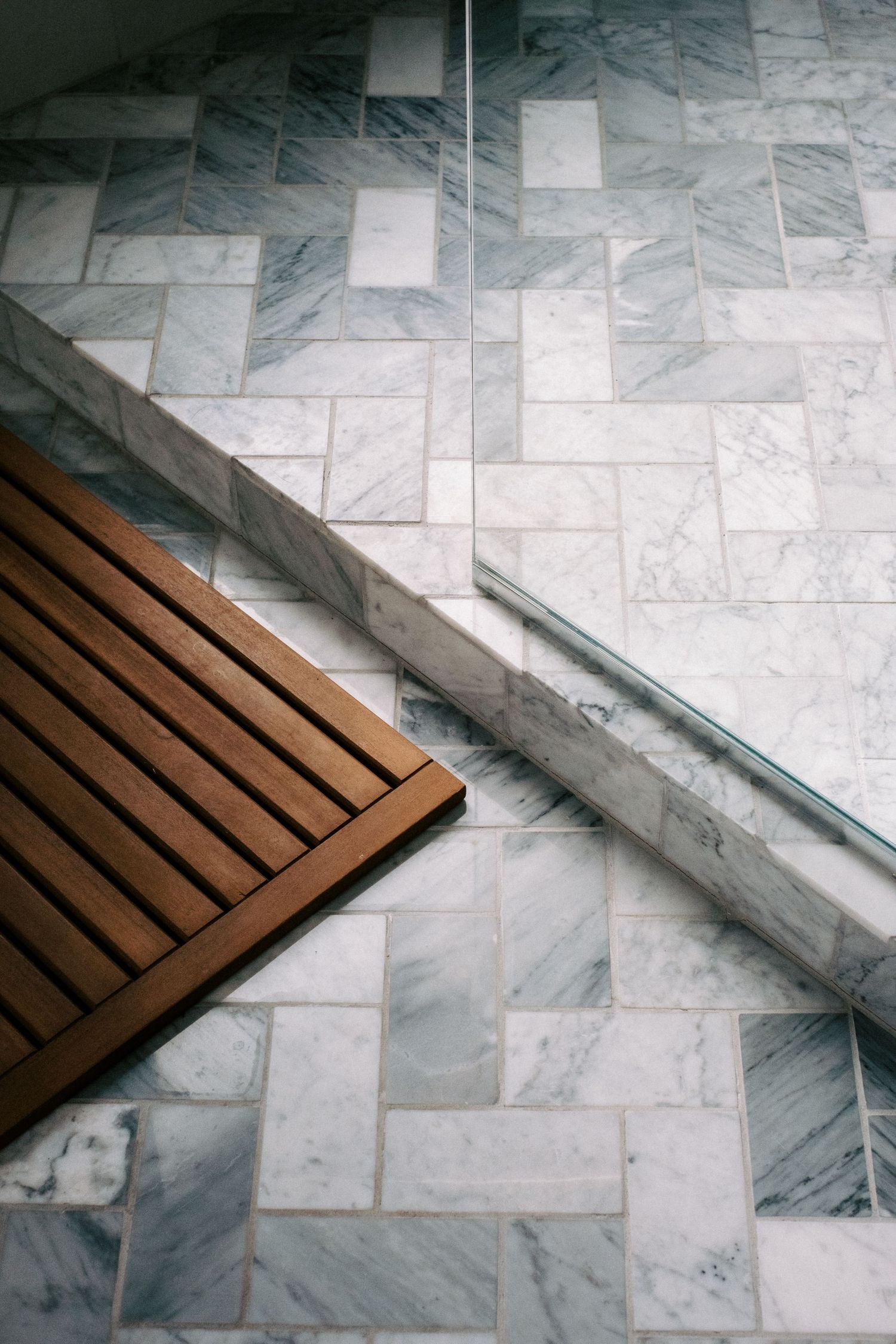 Marble tile flooring with wooden bath mat creating elegant bathroom detail.