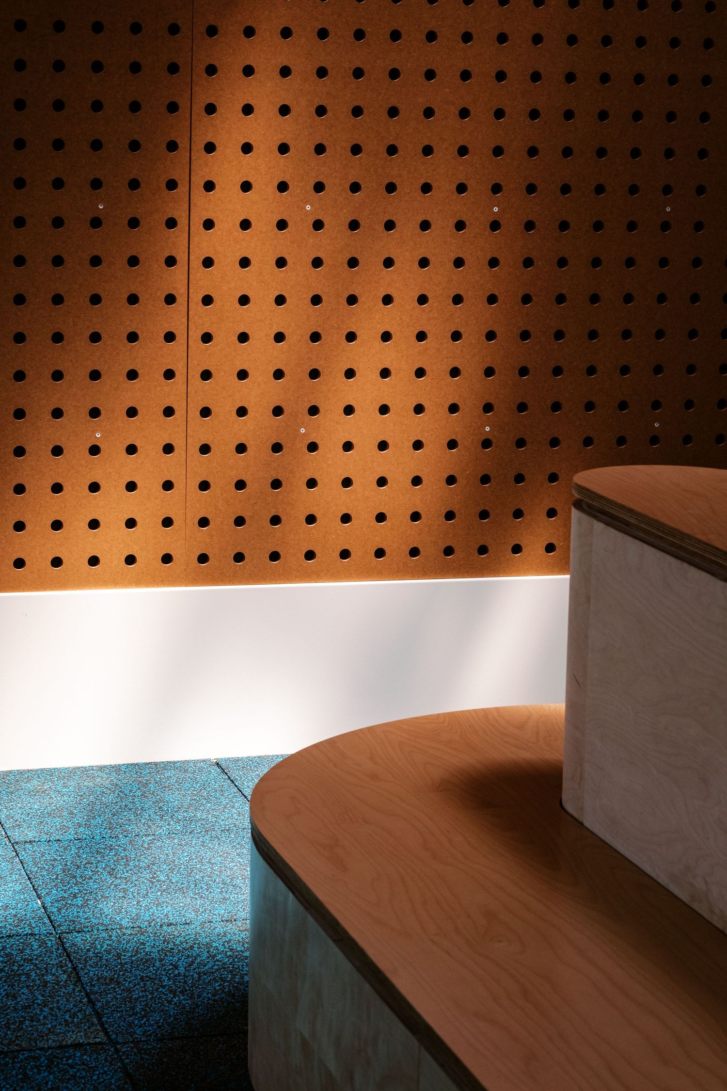 Perforated wooden wall panel with dramatic lighting casting shadows on a blue floor.