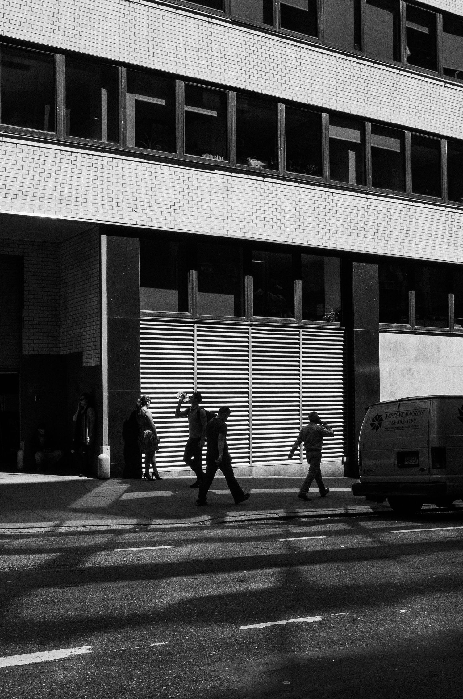 Black and white urban street scene with silhouettes of people walking past a modern building with striped facade.