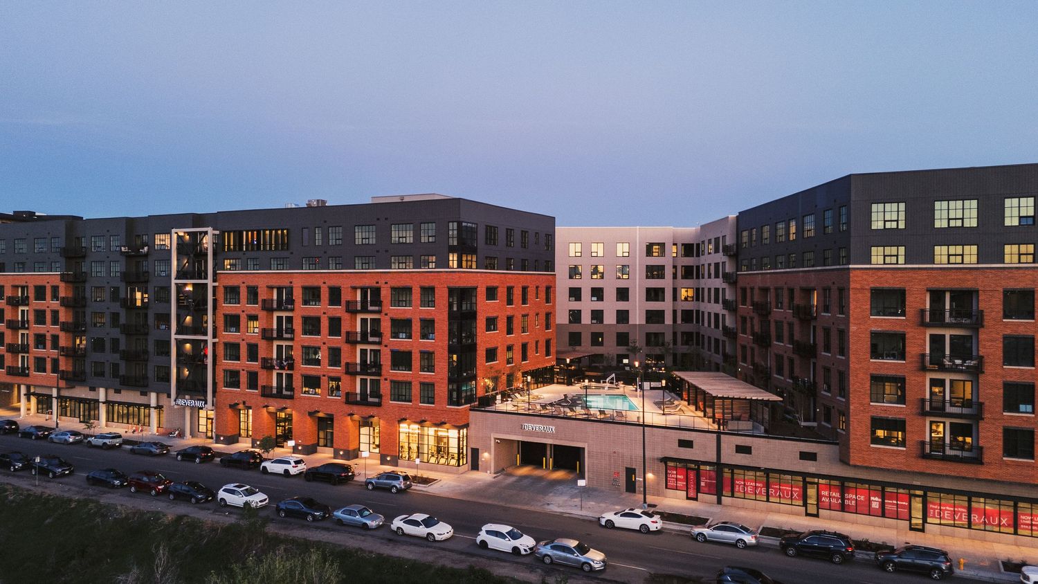 Modern apartment complex with red brick exterior and balconies shown in panoramic view at dusk.