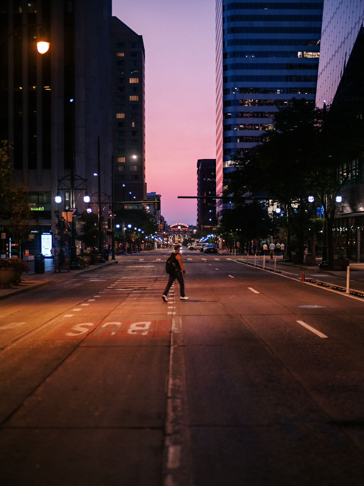 Empty city street at dusk with purple sky and illuminated buildings.