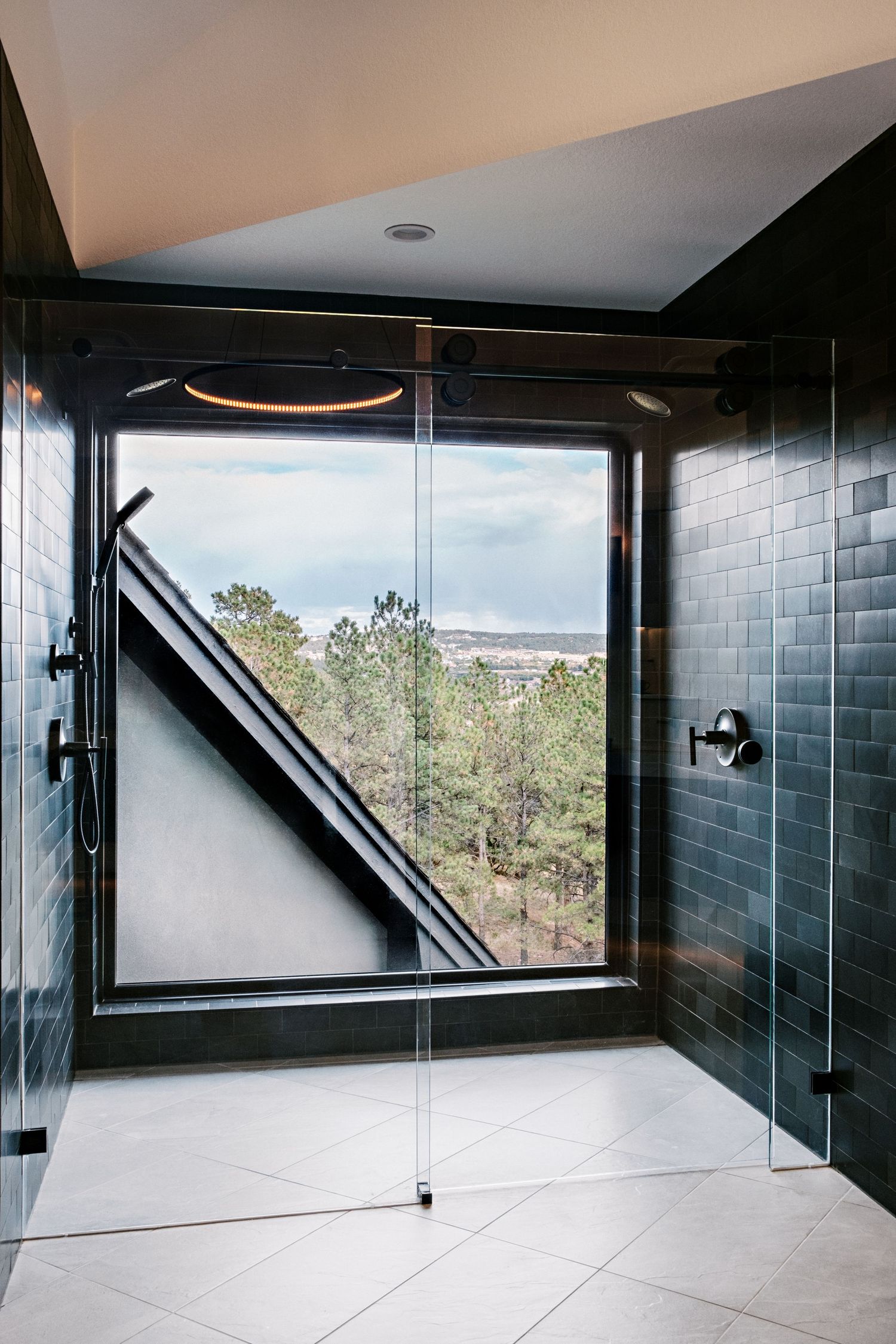 Modern bathroom with dark tile walls and large windows offering scenic mountain views.